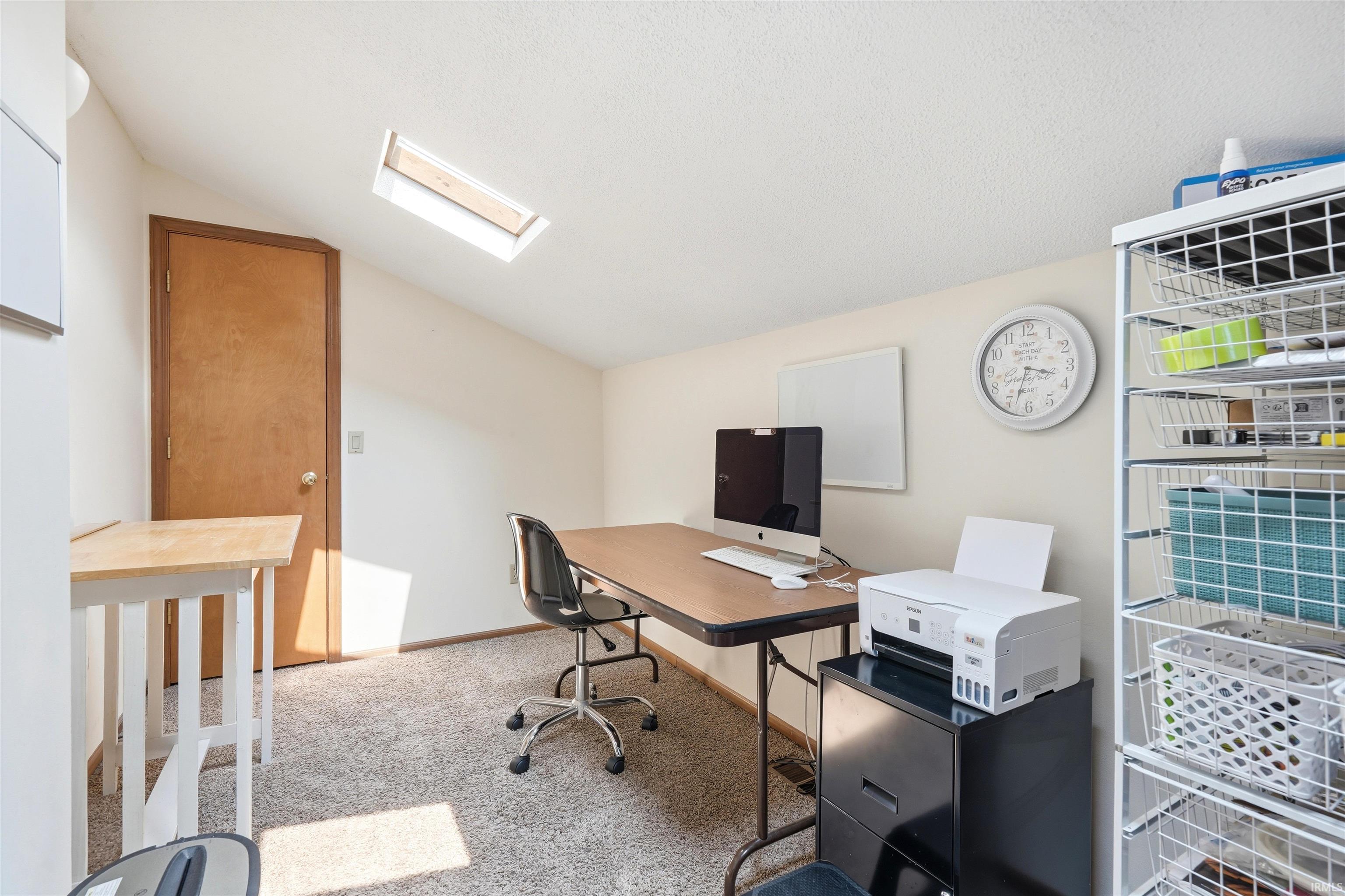 Recessed skylight, sloped ceiling, light-colored wall paint, wood-finish door, and carpeted flooring