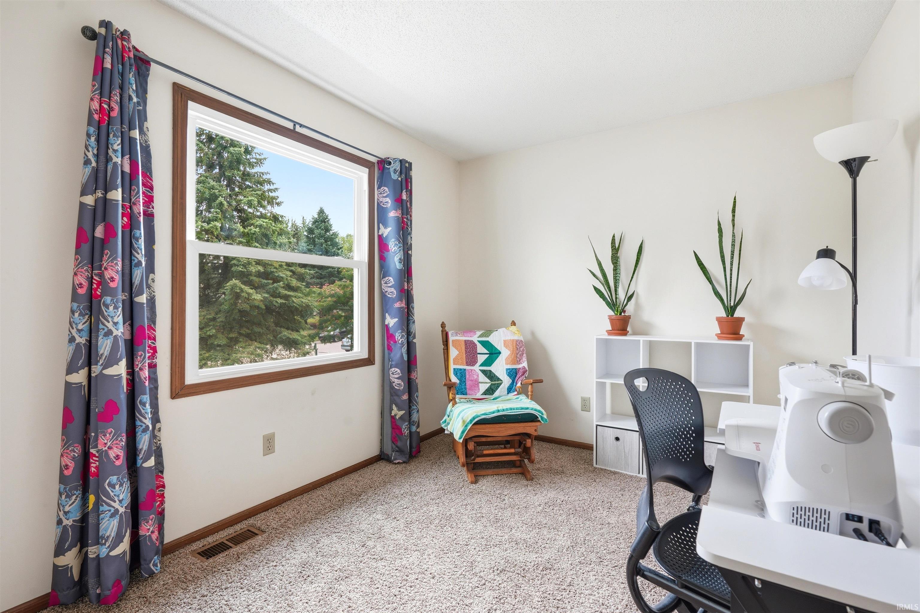 Bright home office featuring large picture window with natural light, neutral carpeting, white built-in cabinetry with open shelving, and black ergonomic desk chair