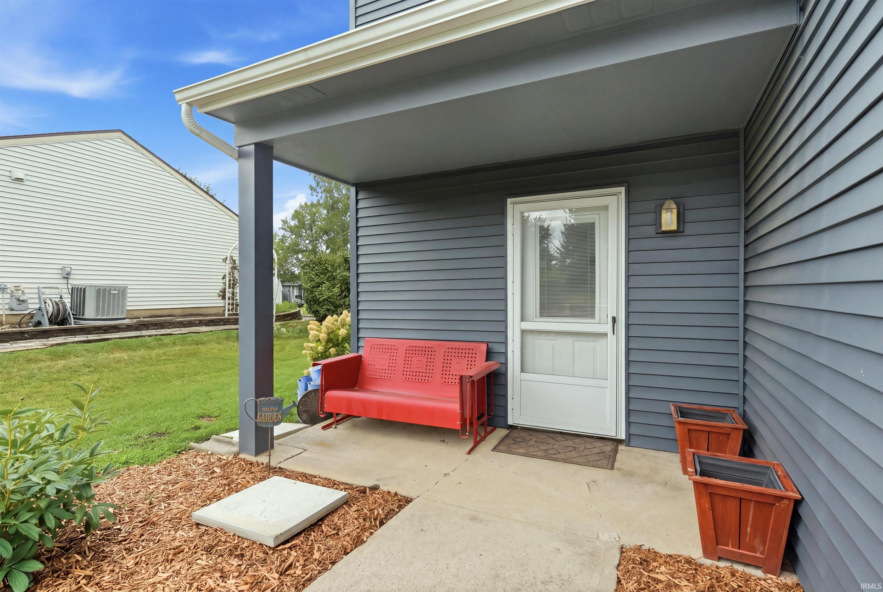 Covered patio with steel support posts and concrete flooring opens directly from the white entry door
