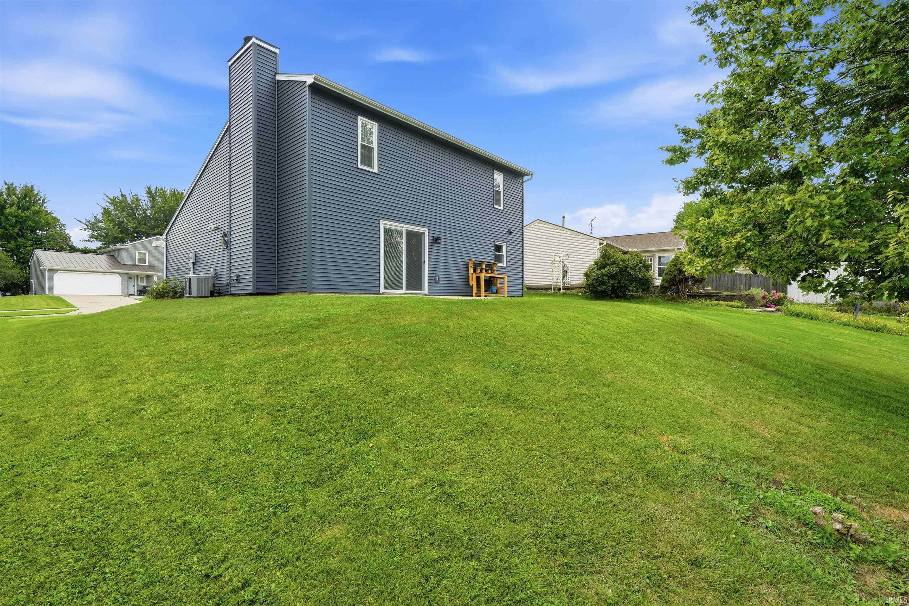 Expansive grassy yard with mature trees and a two-story residence featuring blue siding, white trim, and a prominent chimney