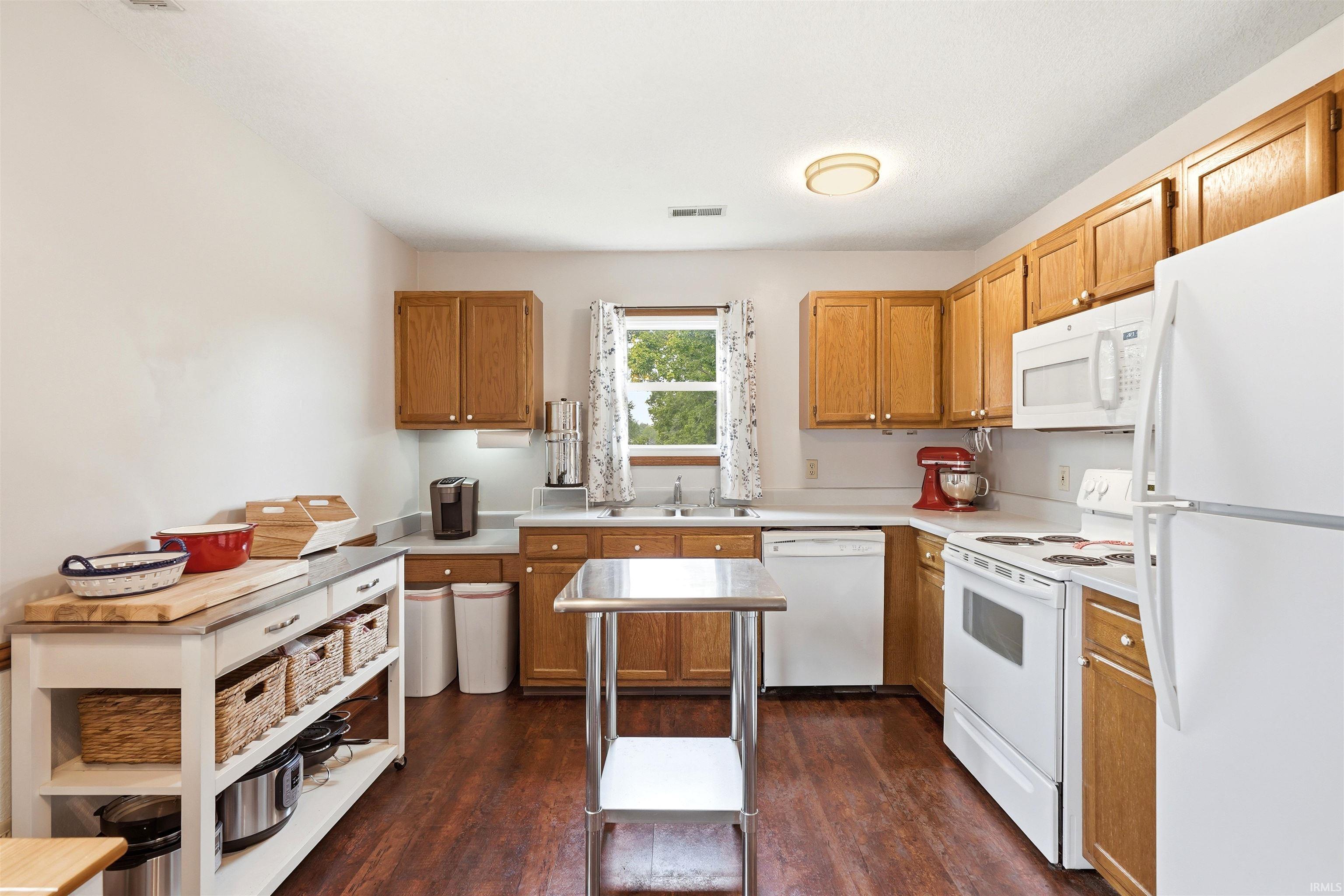 Galley-style kitchen featuring wood-finish cabinetry, white appliances including a refrigerator and electric range, laminate countertops with undermount sink, wood-finish flooring throughout, and a central island with prep space