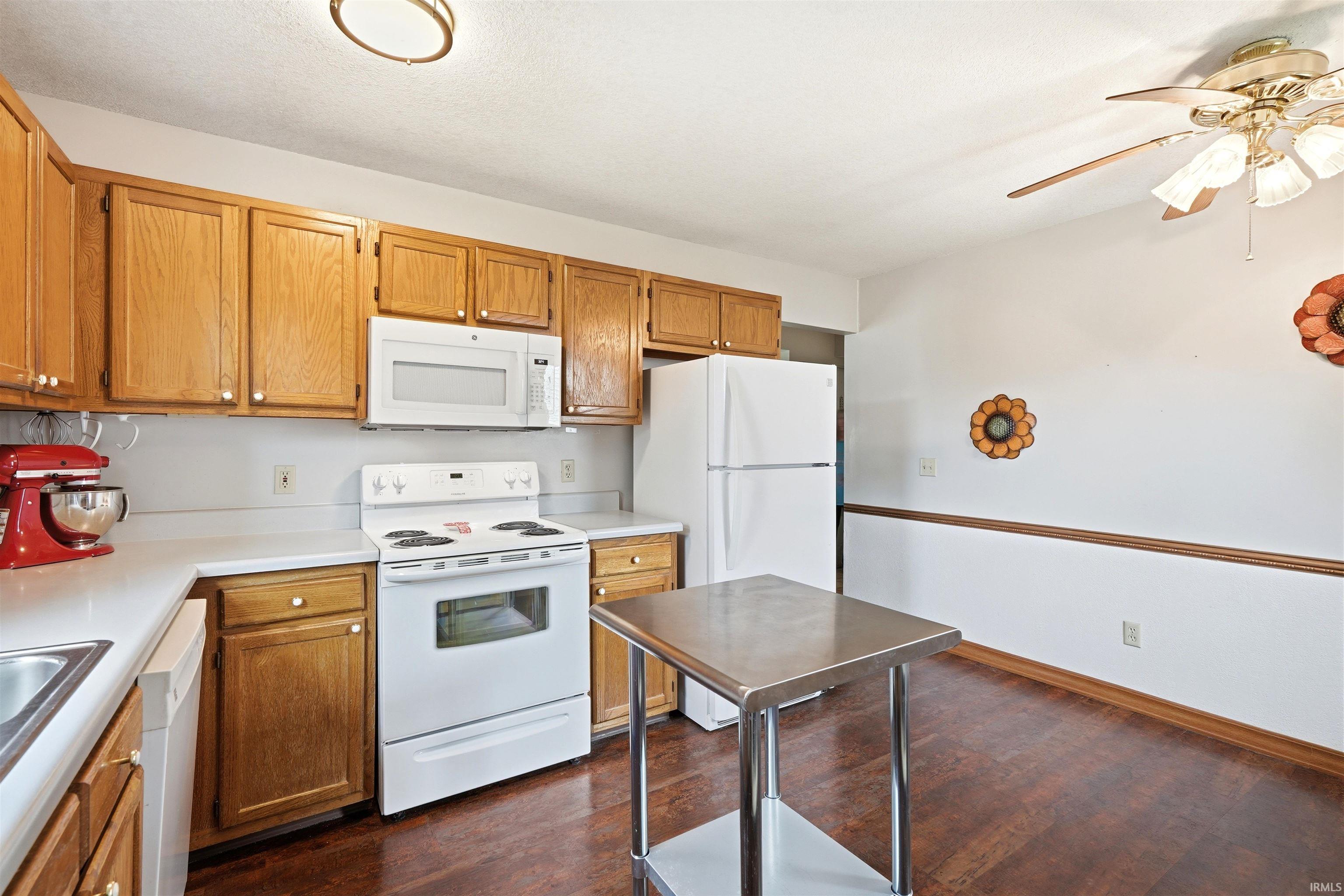 Spacious kitchen featuring warm wood cabinetry, white appliances including a refrigerator and electric range, stainless steel countertops, and ample storage