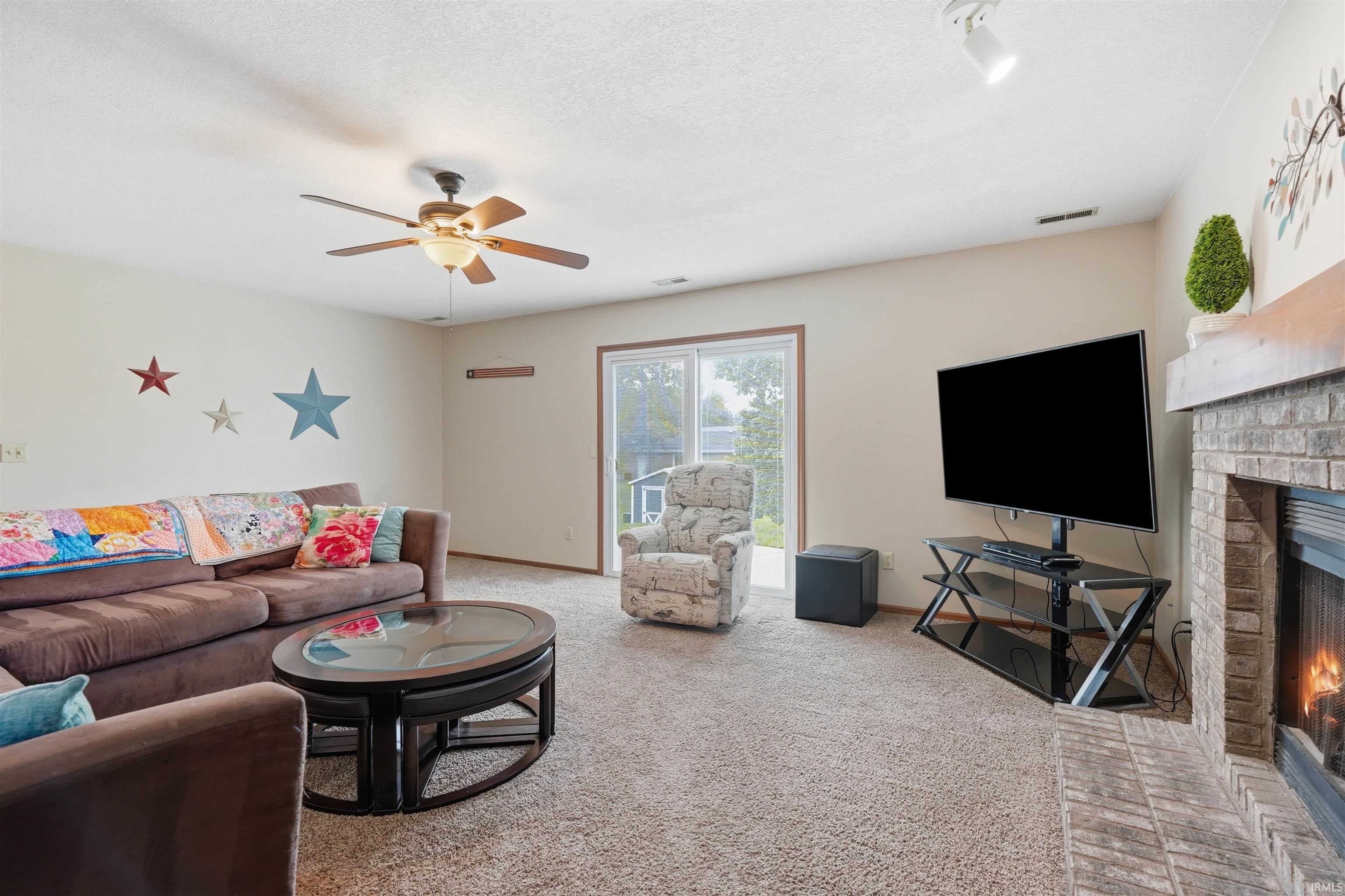 Carpeted living area featuring a ceiling fan, brick fireplace with wood mantel, track lighting, and sliding glass door