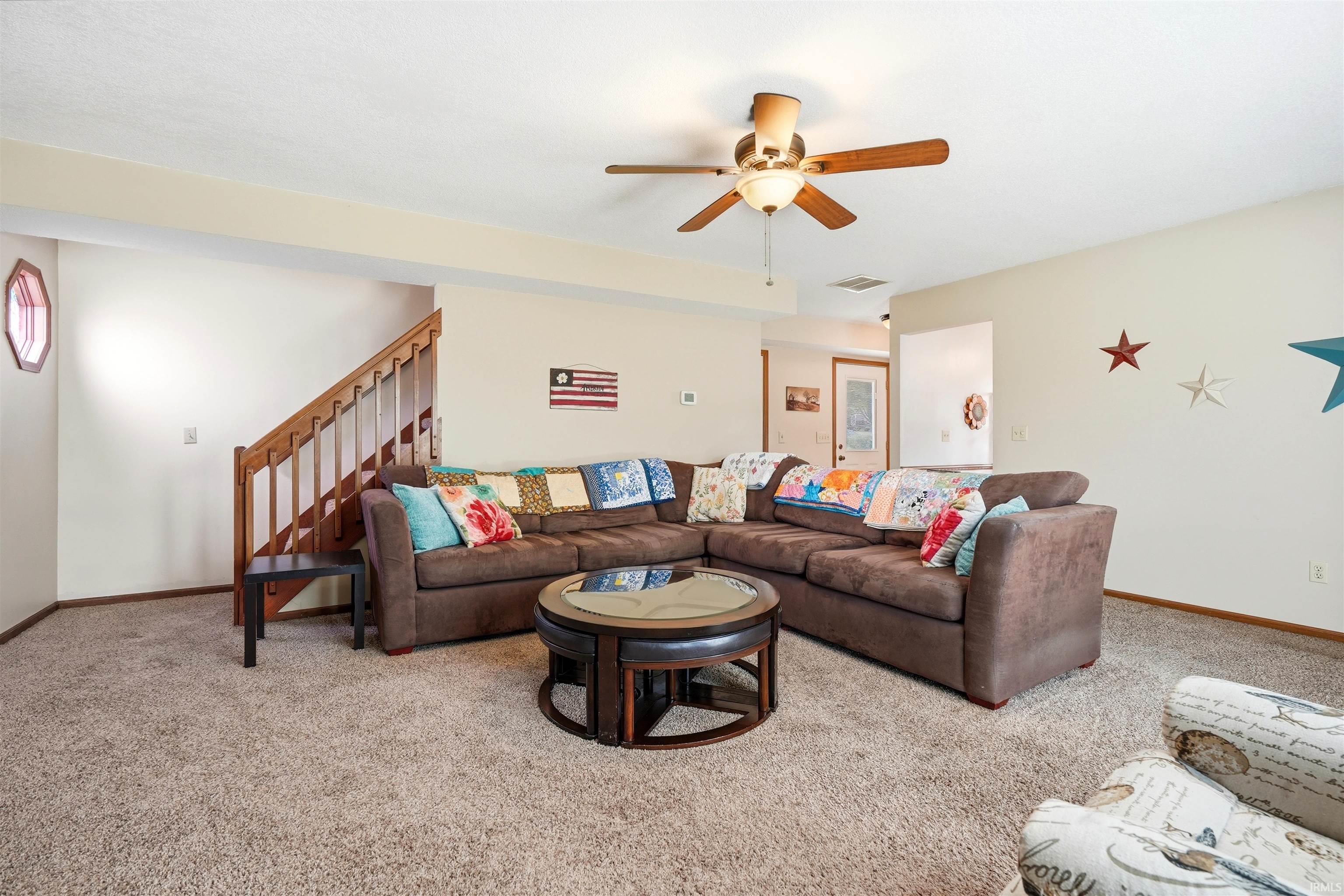 Spacious basement recreation room featuring a sectional layout, neutral carpeting, and a ceiling fan with integrated lighting