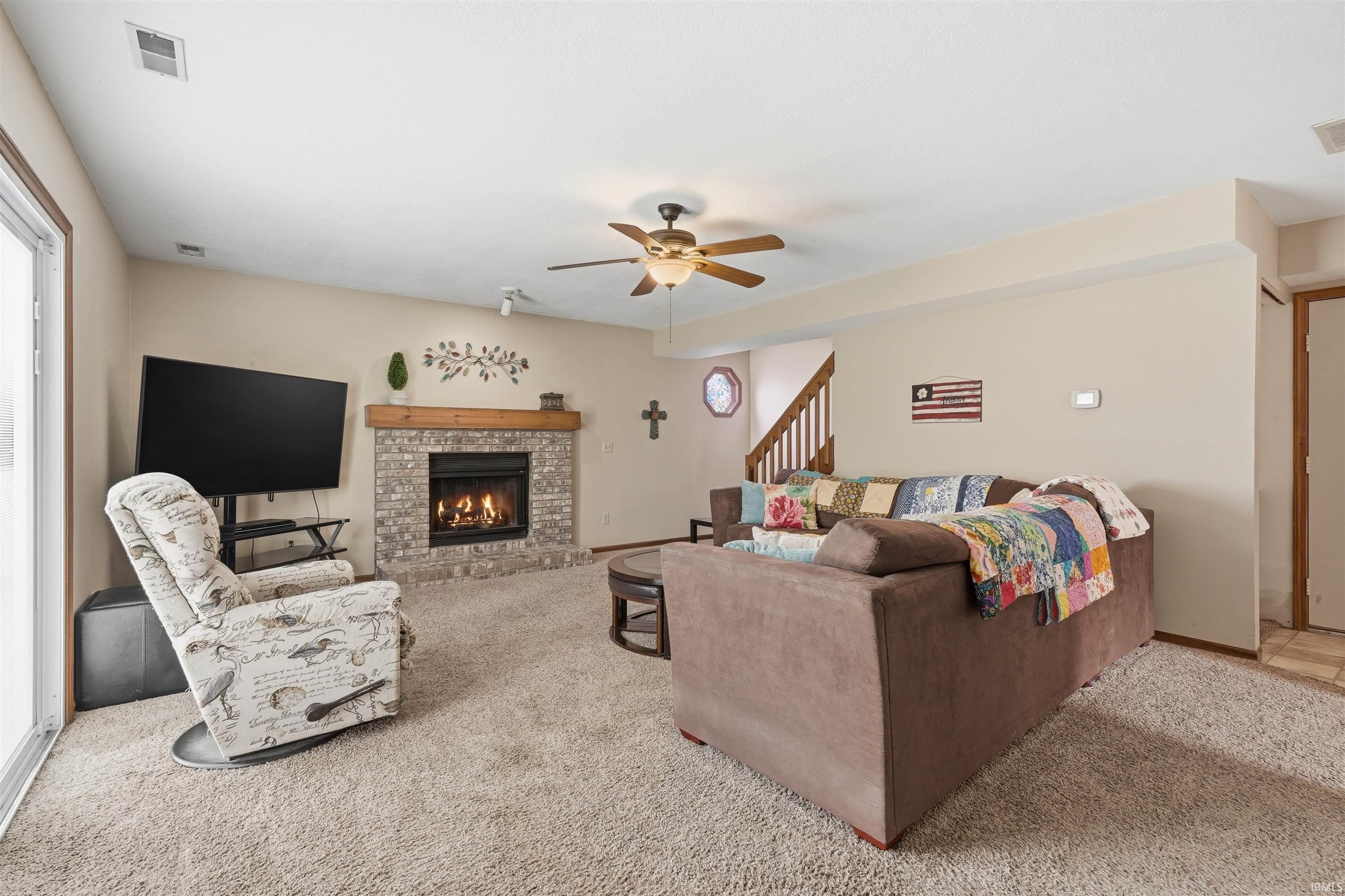 Spacious living area featuring a gas fireplace with stone surround, ceiling fan, and abundant natural light from multiple windows