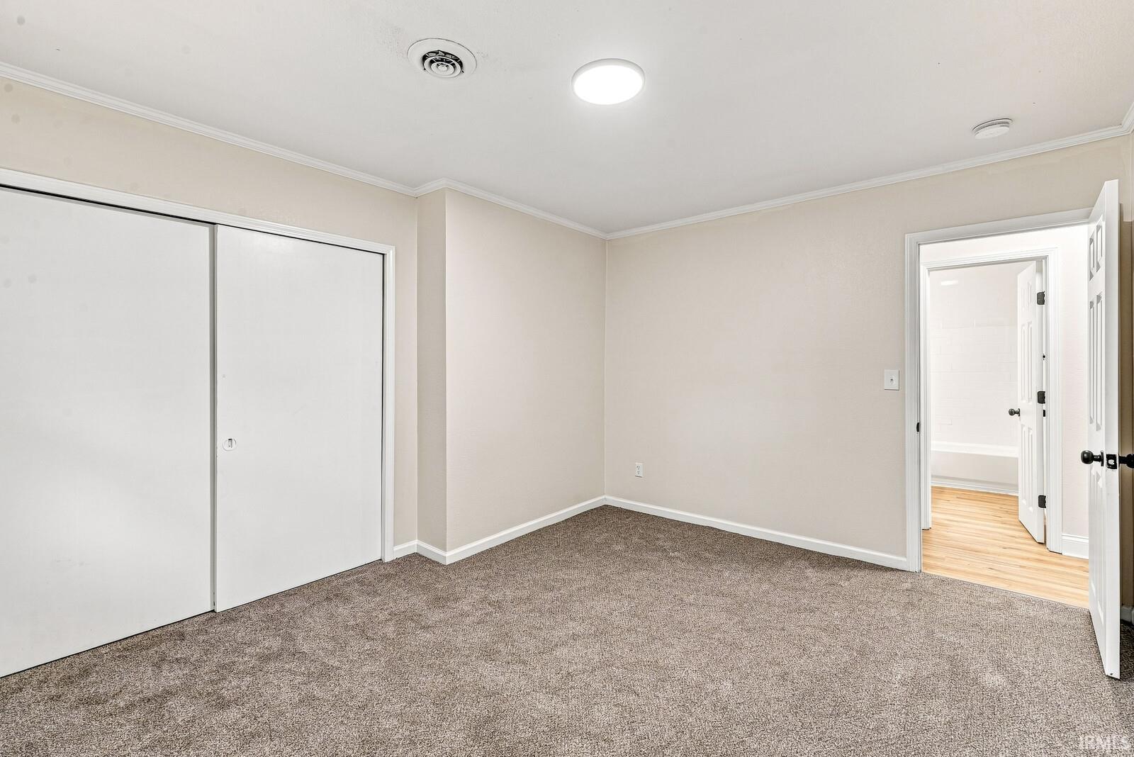 Neutral-toned carpeting, white sliding closet doors, ceiling-mounted lighting, and crown molding