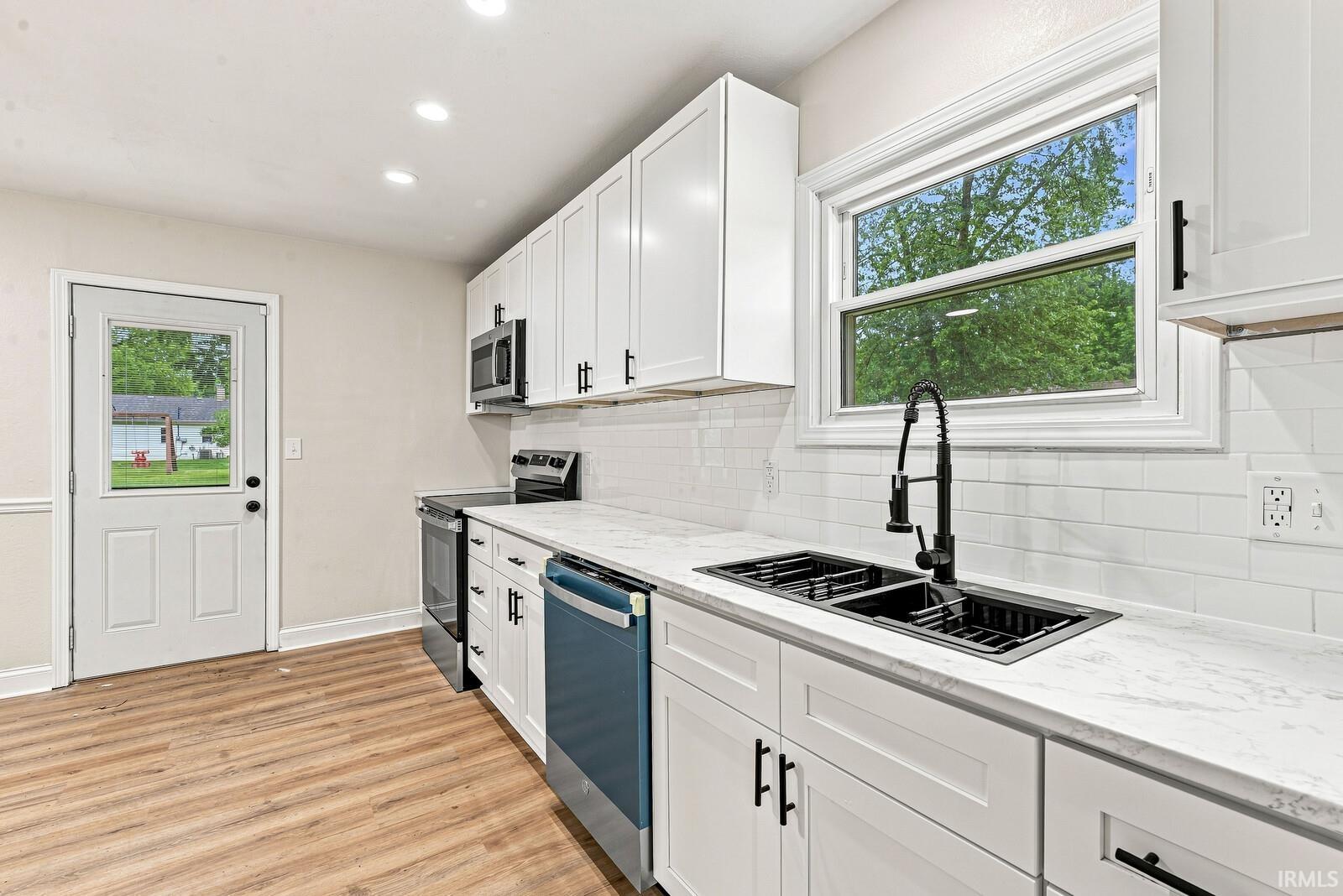 Bright kitchen featuring white cabinetry, stainless steel appliances including a gas range and pull-down faucet, quartz countertops, subway tile backsplash, and abundant natural light from large windows