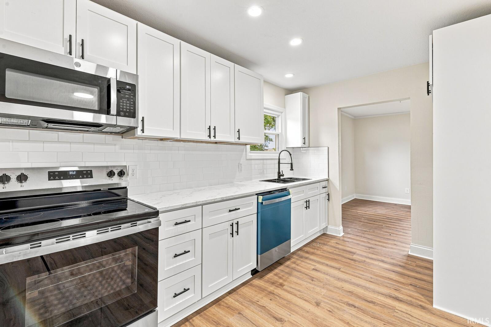 Kitchen featuring white cabinetry with dark hardware, a white subway tile backsplash, white countertops, and wood-finish flooring
