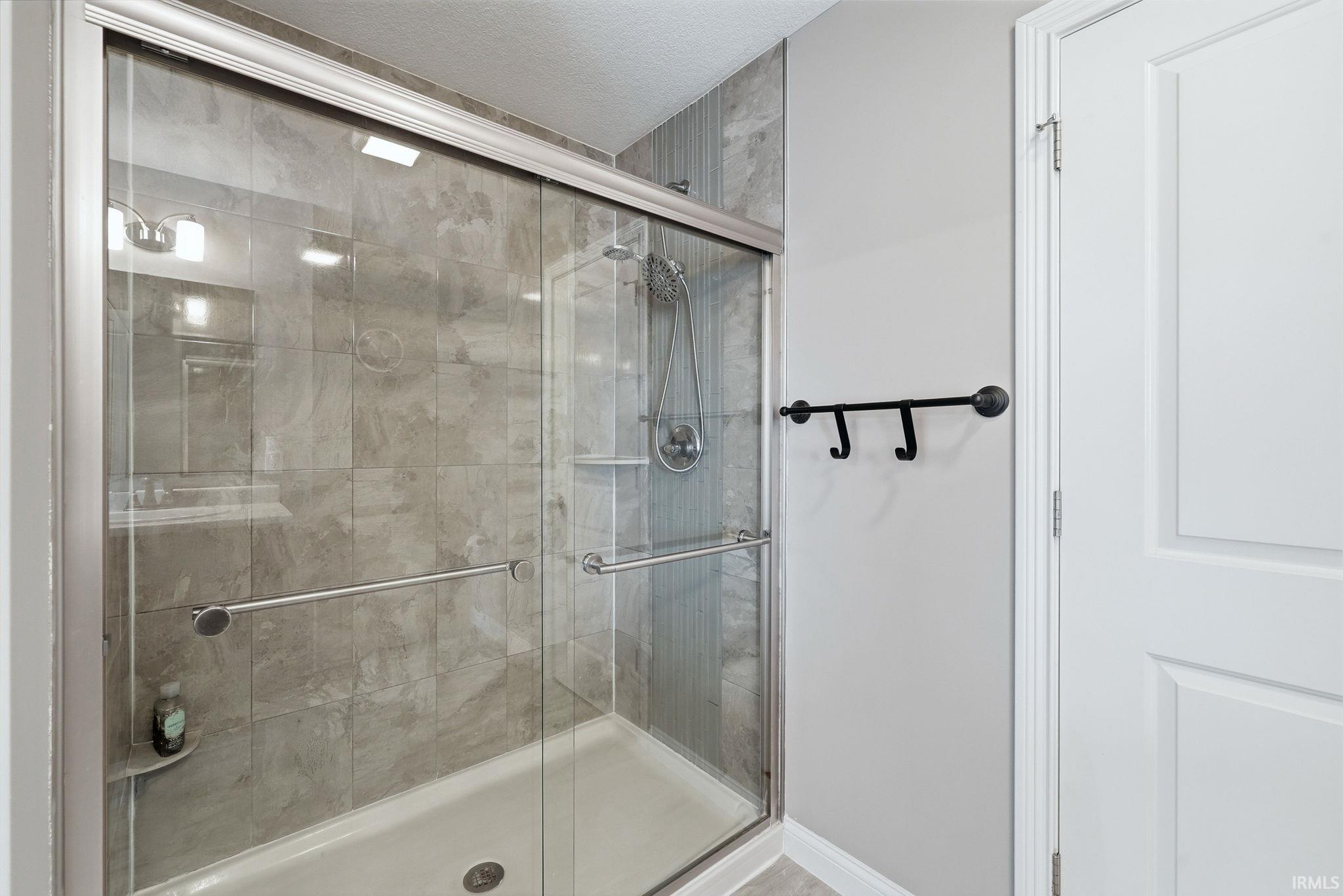 Contemporary shower enclosure featuring frameless glass sliding doors, neutral tile surround with linear layout, integrated showerhead with handheld spray fixture, and a spacious walk-in base