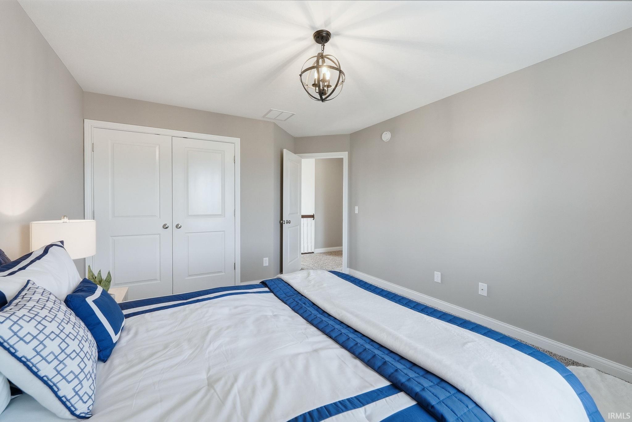 Neutral wall paint, plush carpet flooring, bi-fold closet doors, and an overhead orb chandelier
