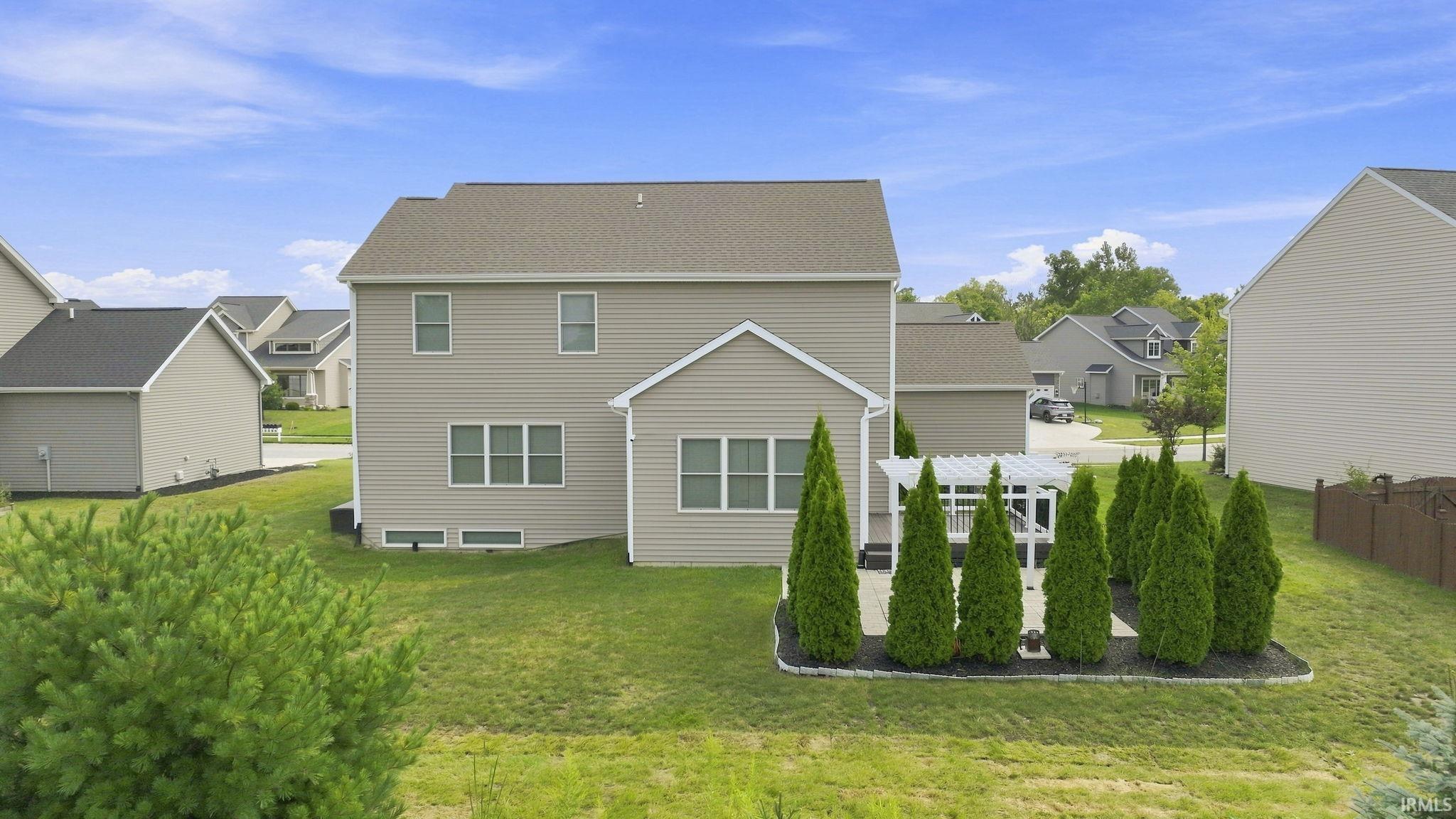 Exterior siding residence featuring a patio with a white pergola, a surrounding arrangement of evergreen trees, and a grassy lawn