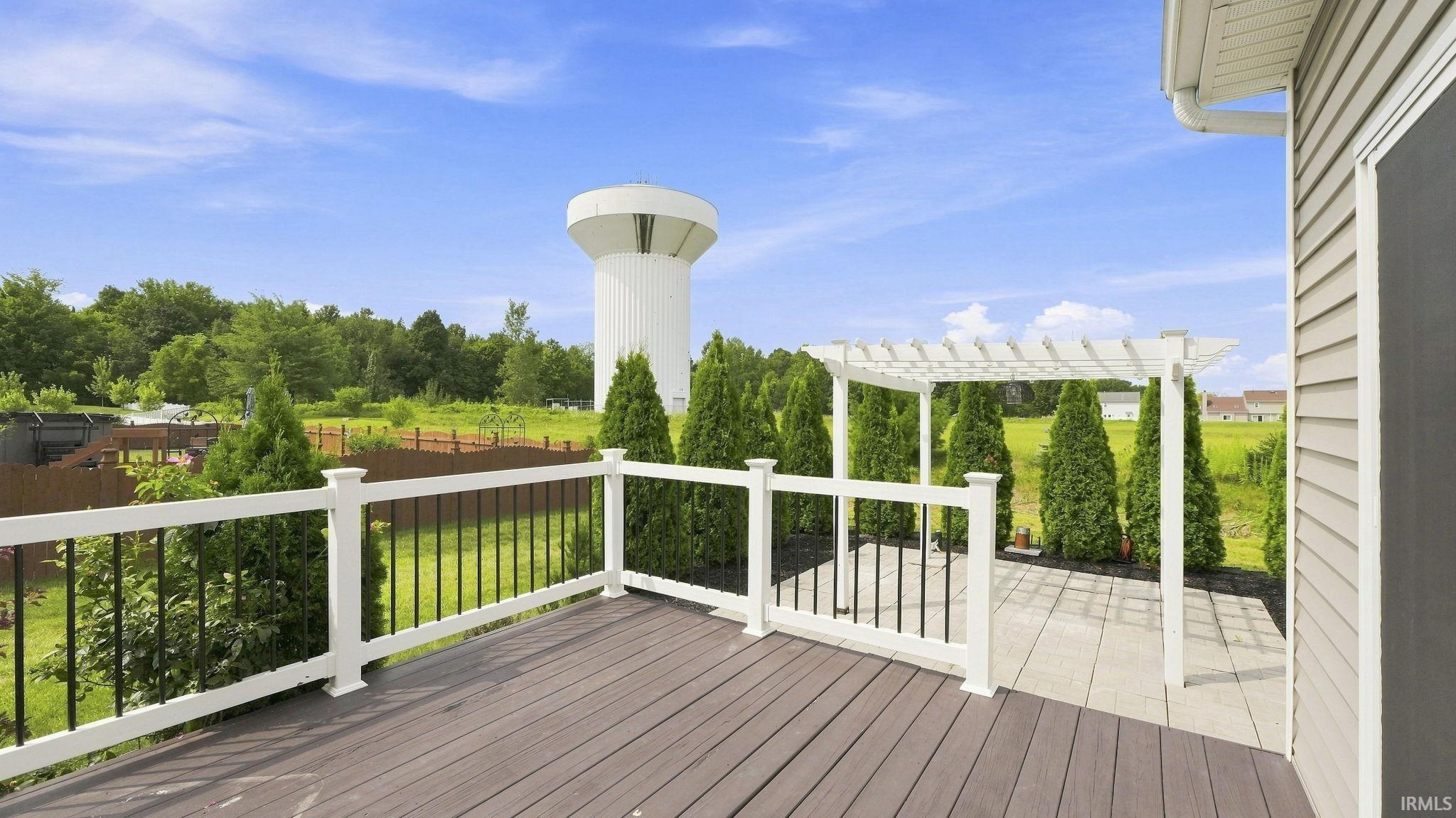 Expansive outdoor living area featuring a wood-finish deck, white railing, and a patio with a white pergola