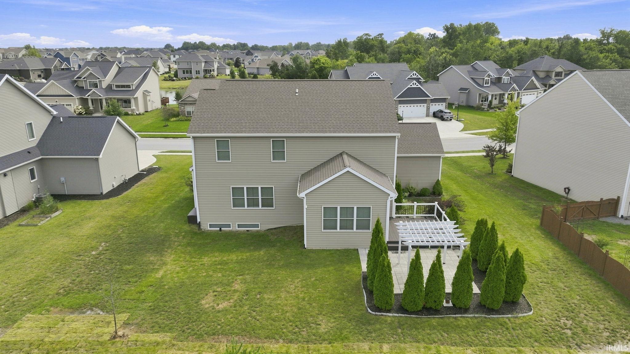 Expansive rear exterior featuring a concrete patio, white pergola, and manicured landscaping with evergreen shrubs