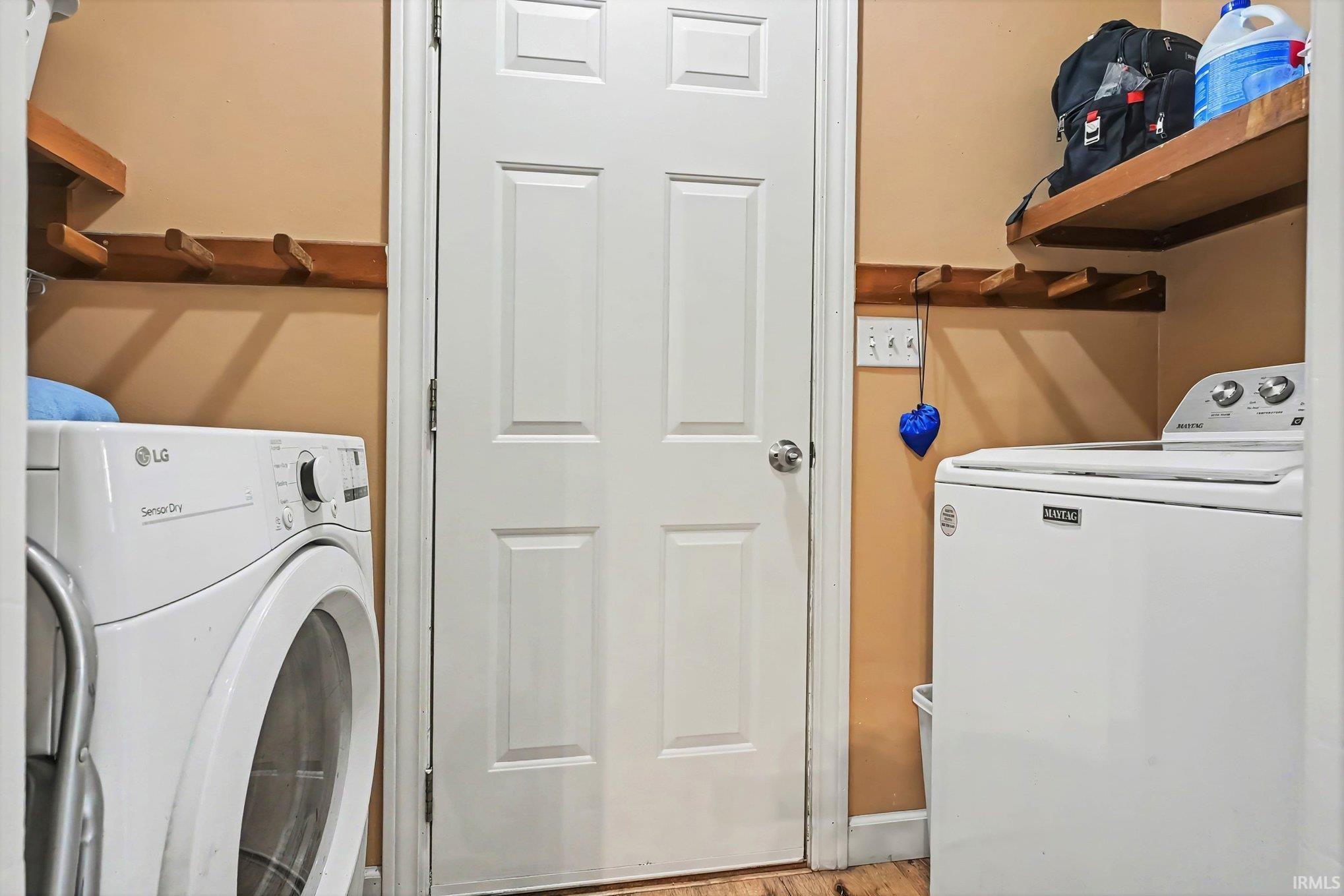 Laundry area featuring wood-finish flooring, overhead shelving, and a paneled door