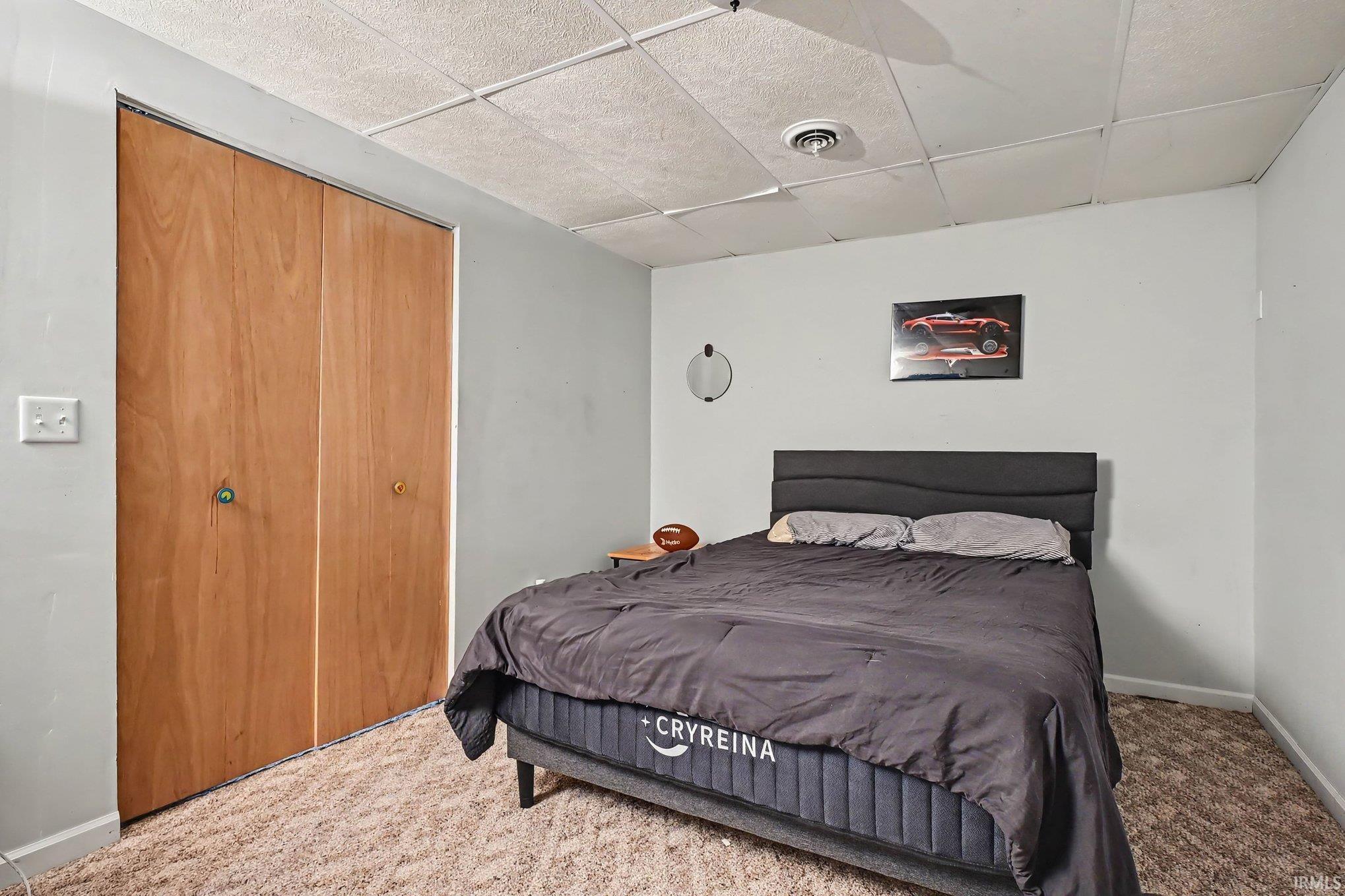 Wood-finish bi-fold closet doors, textured ceiling panels, and light-colored wall paint