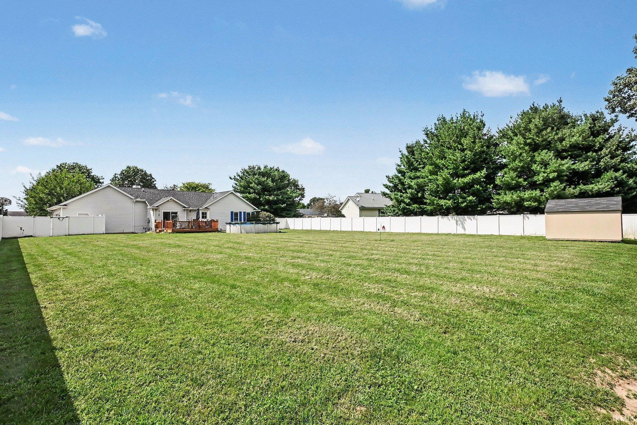 Expansive grassy yard with full vinyl fencing and a detached storage shed