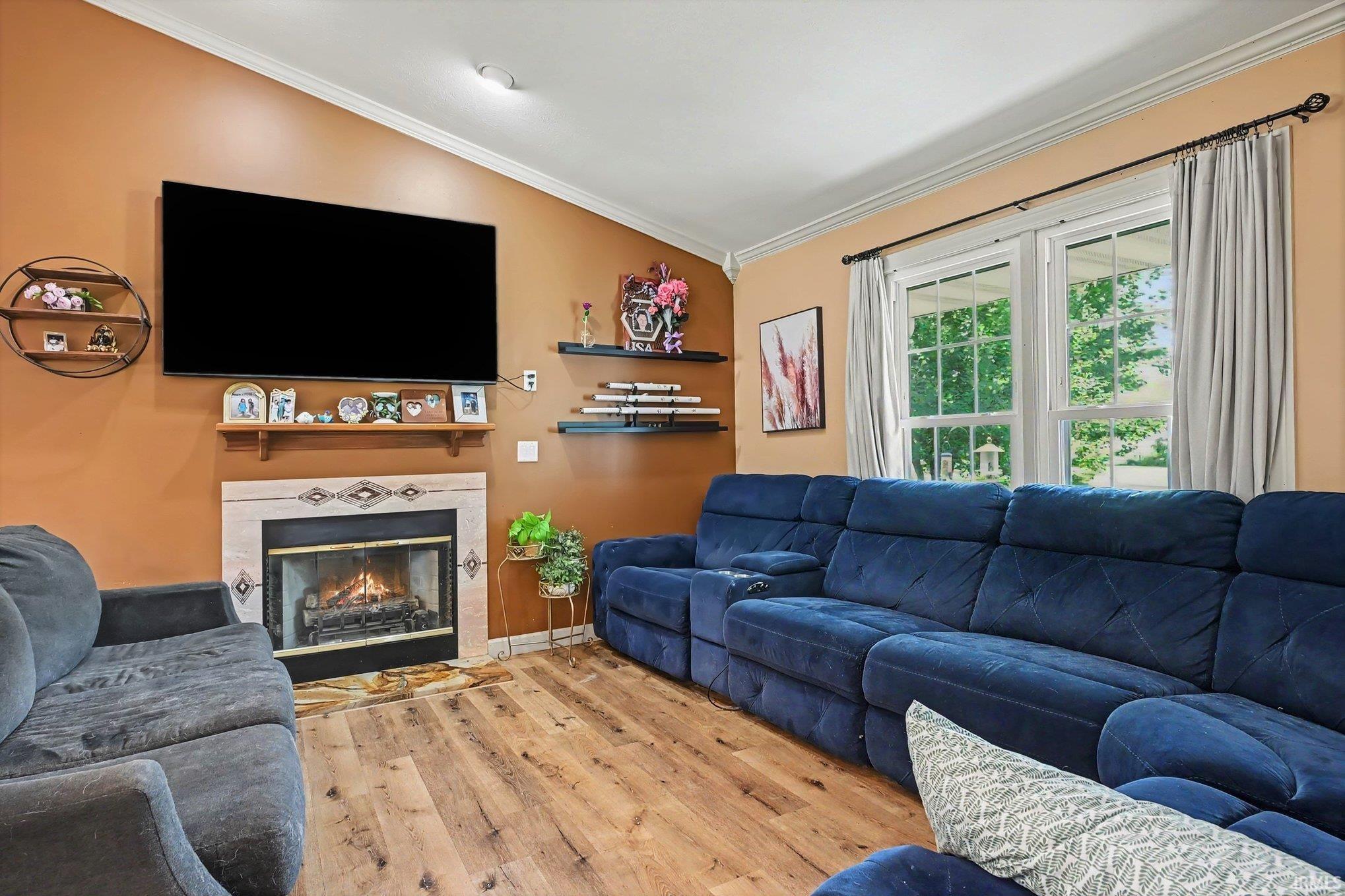 Vaulted ceiling with an integrated light fixture, wood-finish flooring, and a fireplace with a decorative tile surround and mantel