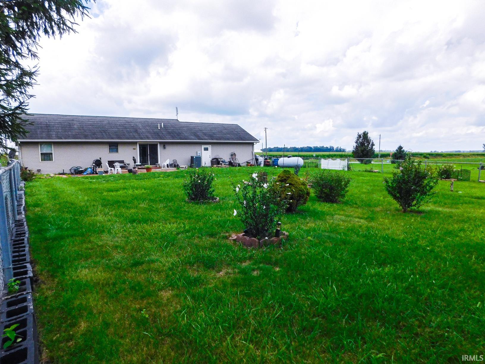 Expansive grassy yard with mature shrubs and trees, featuring a visible section of a chain link fence