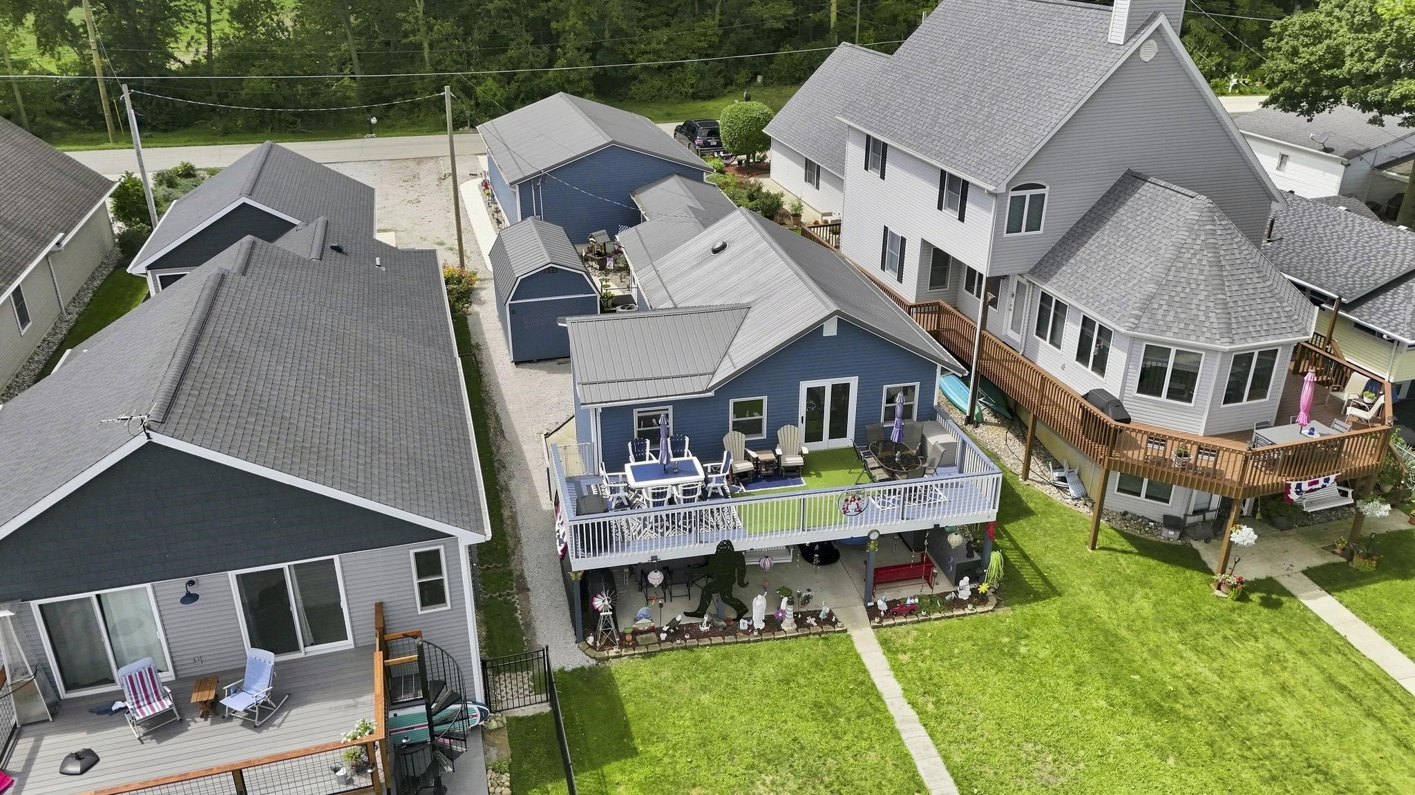 Blue siding exterior featuring a metal roof, an elevated rear deck, a ground-level patio, and an expansive lawn