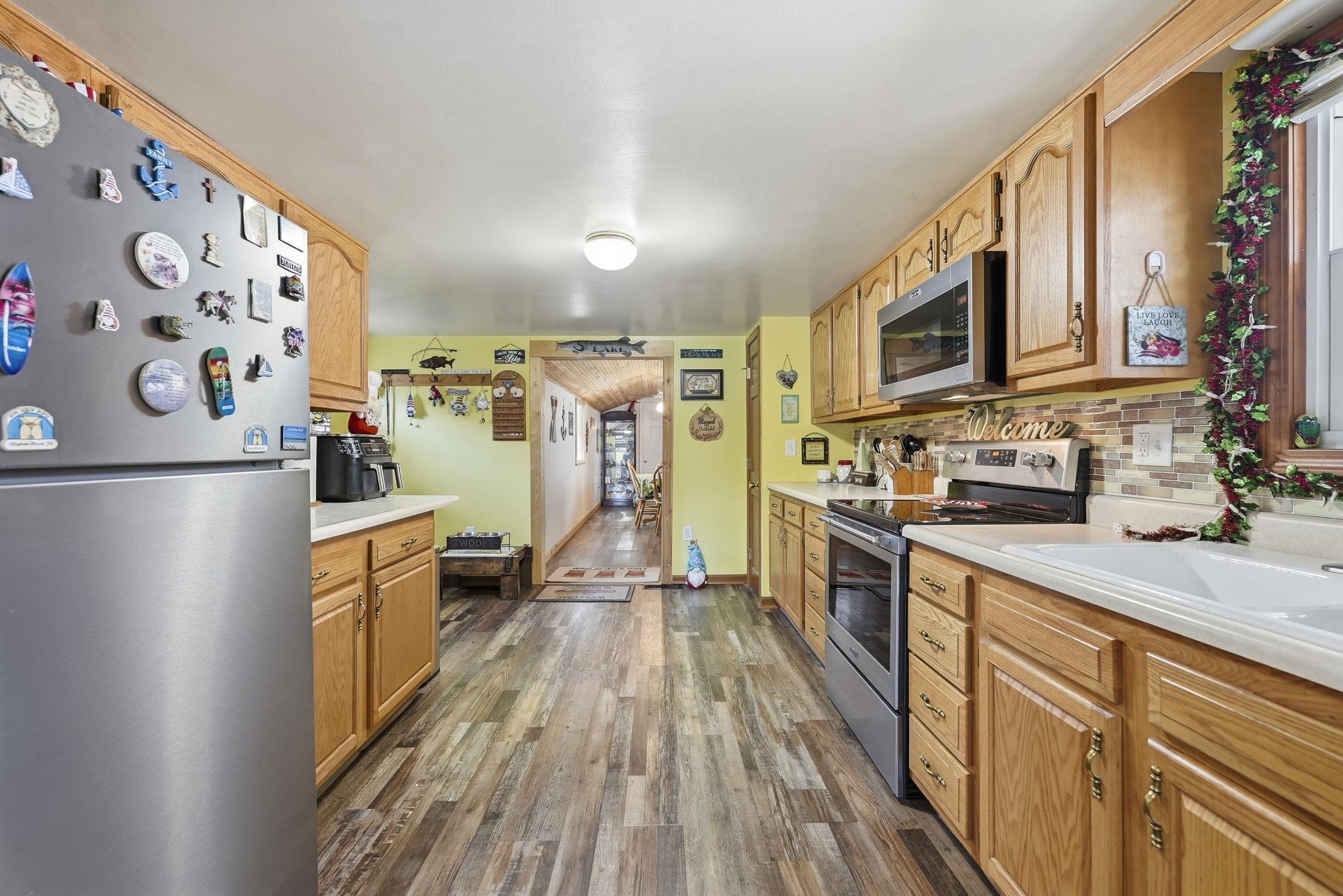 Wood-finish flooring, light wood cabinetry, stainless steel appliances, and a tiled backsplash