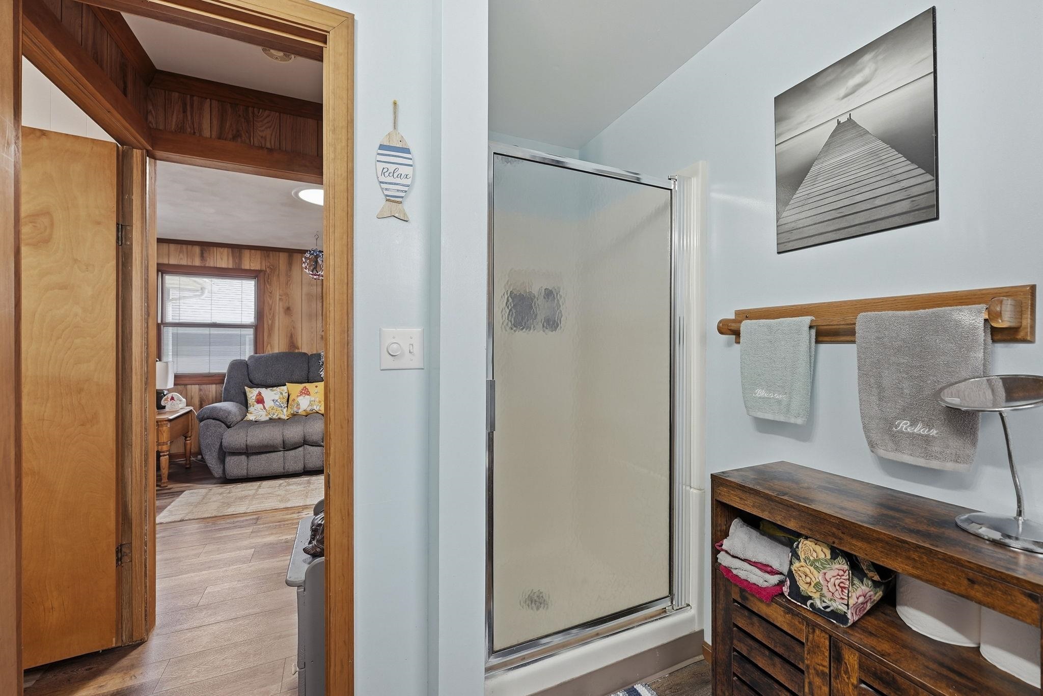 Enclosed shower stall with a clear glass door, a wooden towel bar, and a wooden storage cabinet