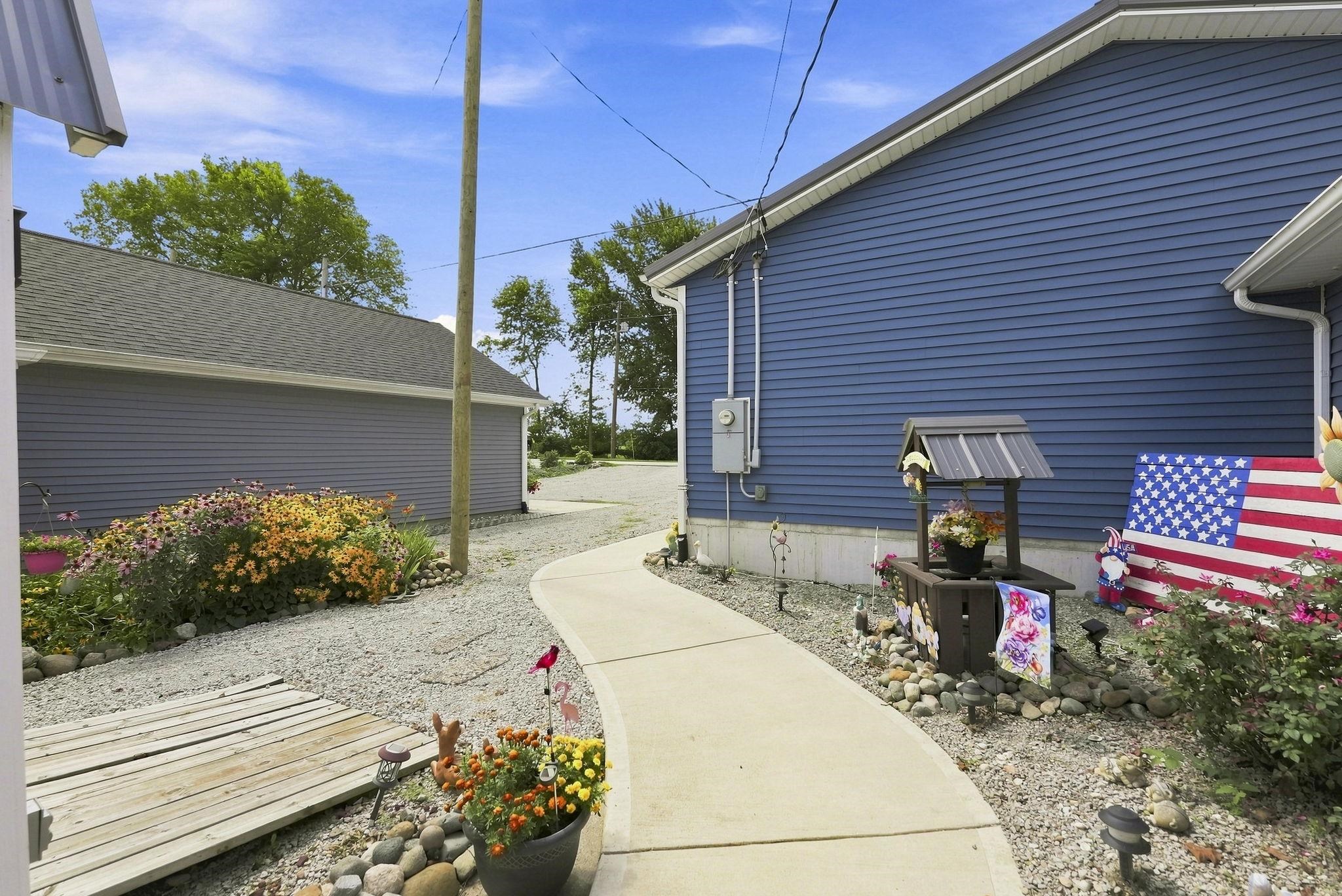 Blue horizontal siding, concrete walkway, gravel landscaping, established plantings, and gray shingle roofing
