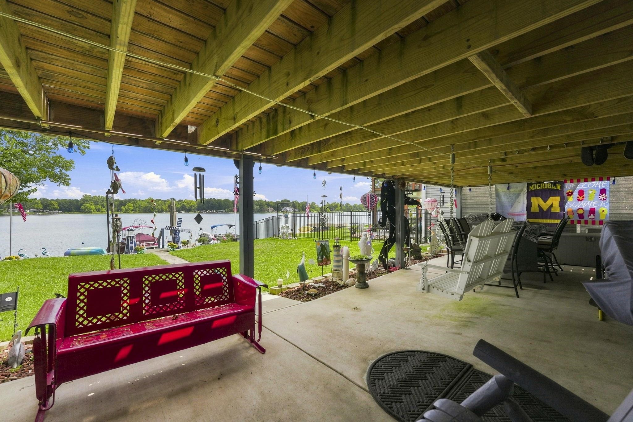 Expansive covered patio with exposed beam ceiling and concrete flooring overlooking manicured lawn and waterfront