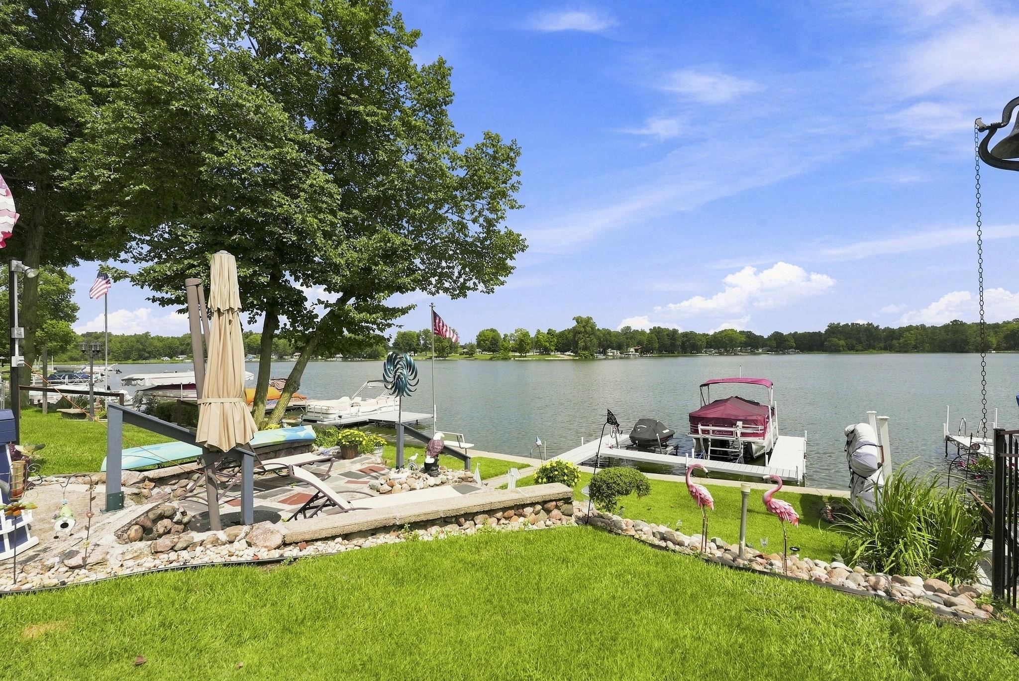 Waterfront property featuring manicured lawn, mature shade trees, and direct water access with dock and boathouse