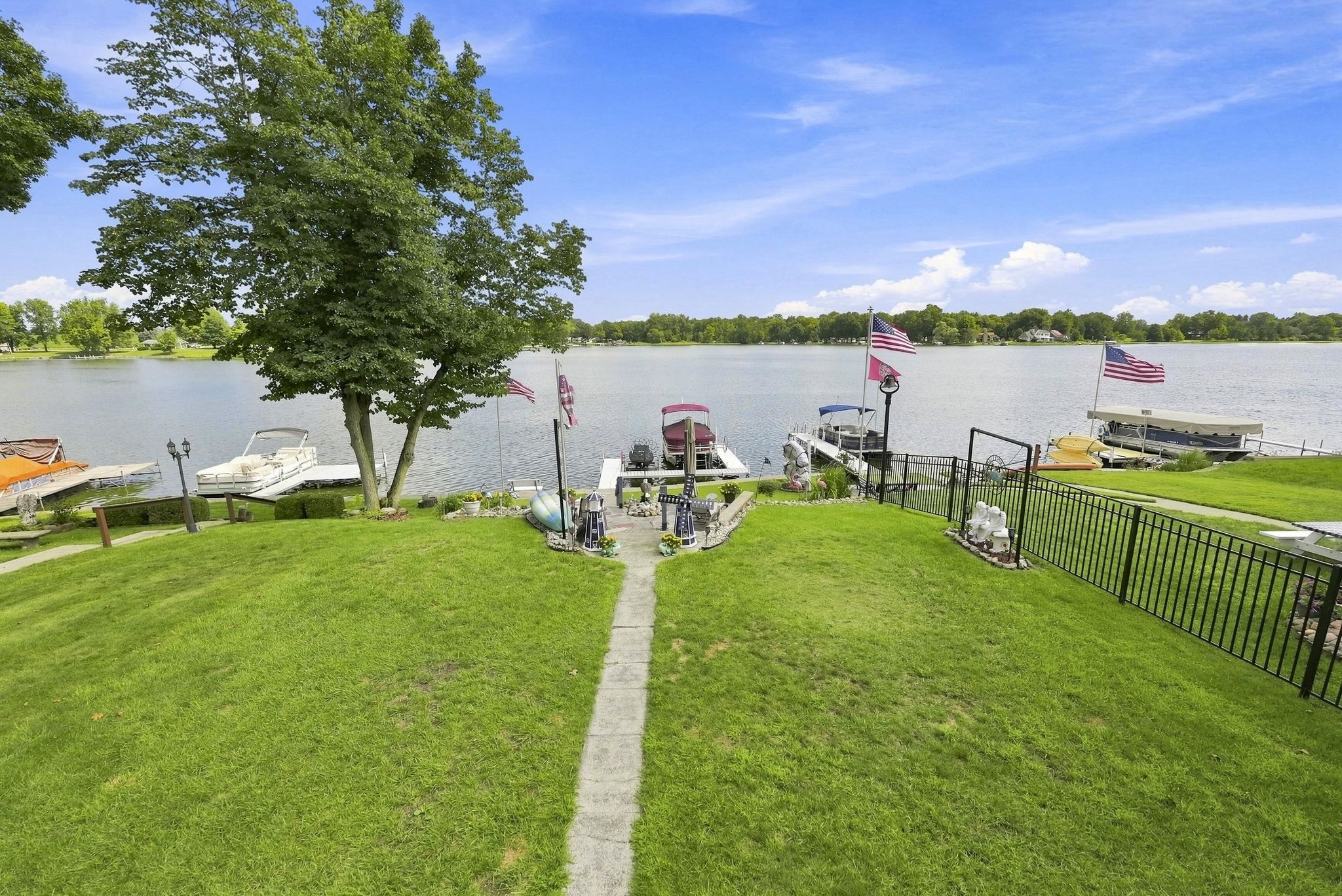 Waterfront property featuring expansive manicured lawn with mature shade trees, private boat dock with multiple slips, black iron fencing, and direct water access ideal for boating enthusiasts