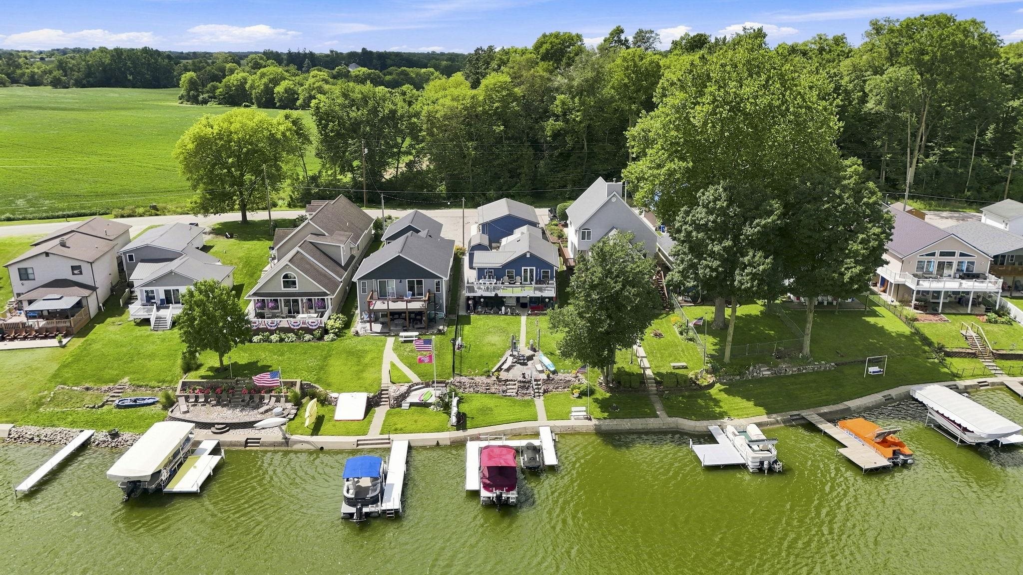 Waterfront property featuring private docks, expansive green lawn, mature trees, and multiple residences