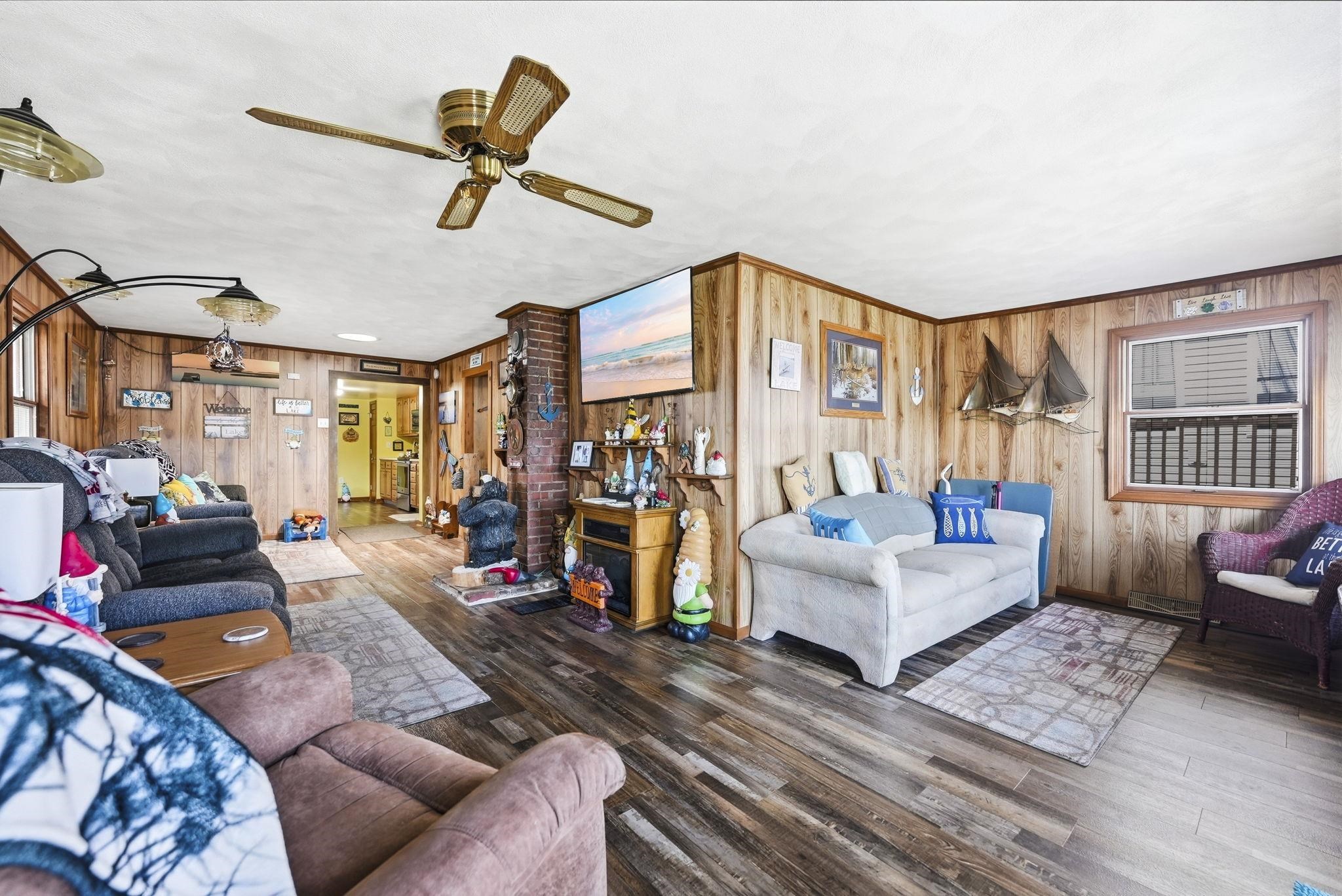 Wood-finish flooring, wood paneling, brick-clad column, ceiling fan, and a window air conditioning unit