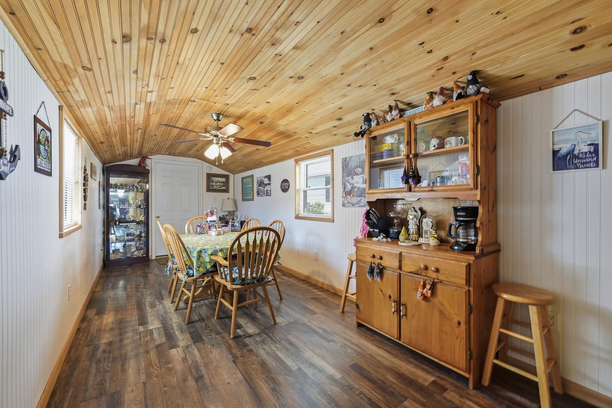 Wood-finish flooring, wood-paneled ceiling, ceiling fan, white paneled walls, and multiple windows