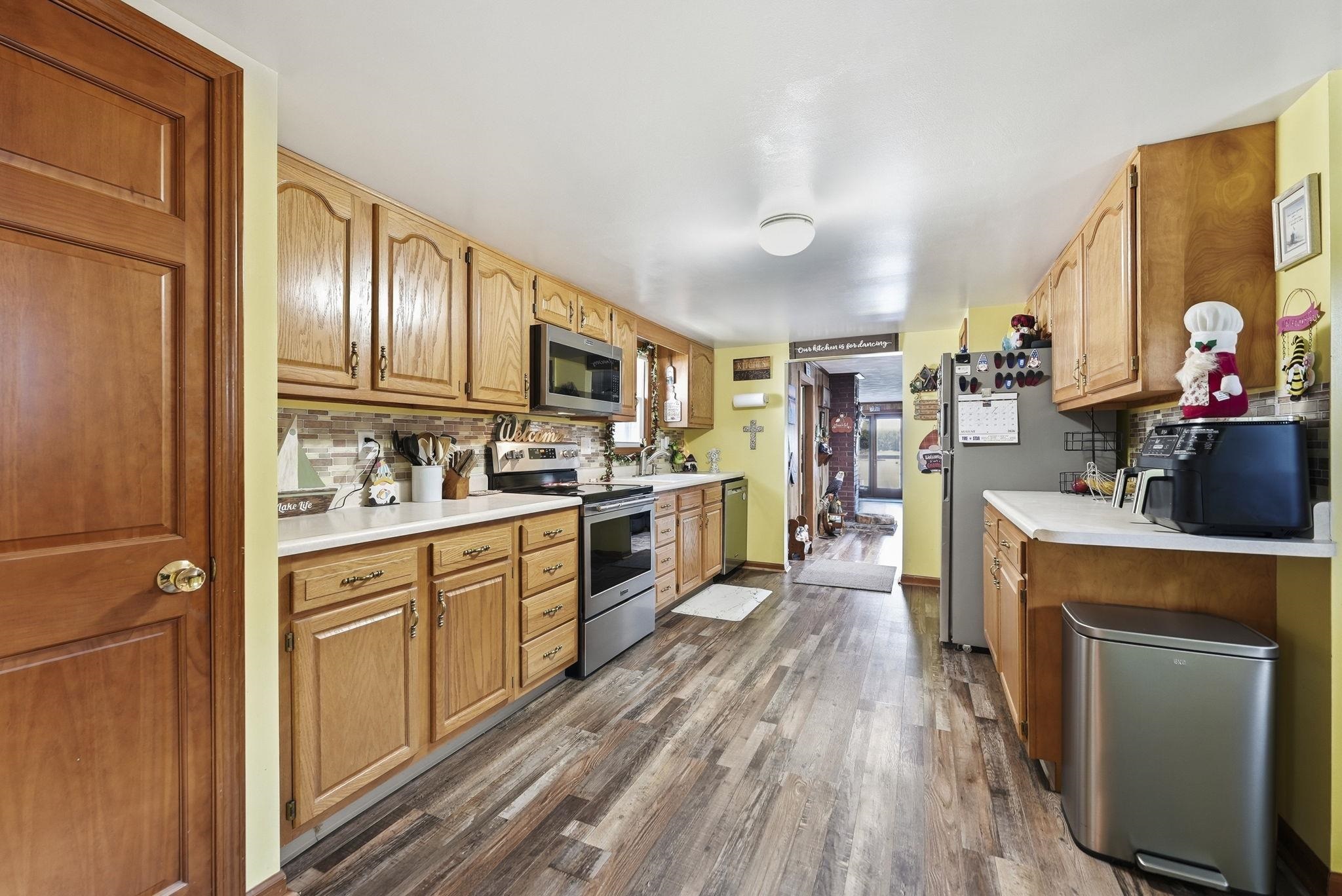 Wood-finish flooring, wood cabinetry, stainless steel appliances, white countertops, and a patterned backsplash