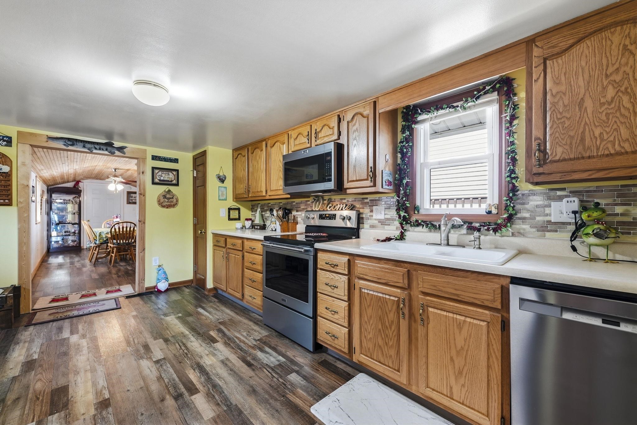Galley-style kitchen featuring wood cabinetry, stainless steel appliances, white subway tile backsplash, and wood-finish flooring throughout