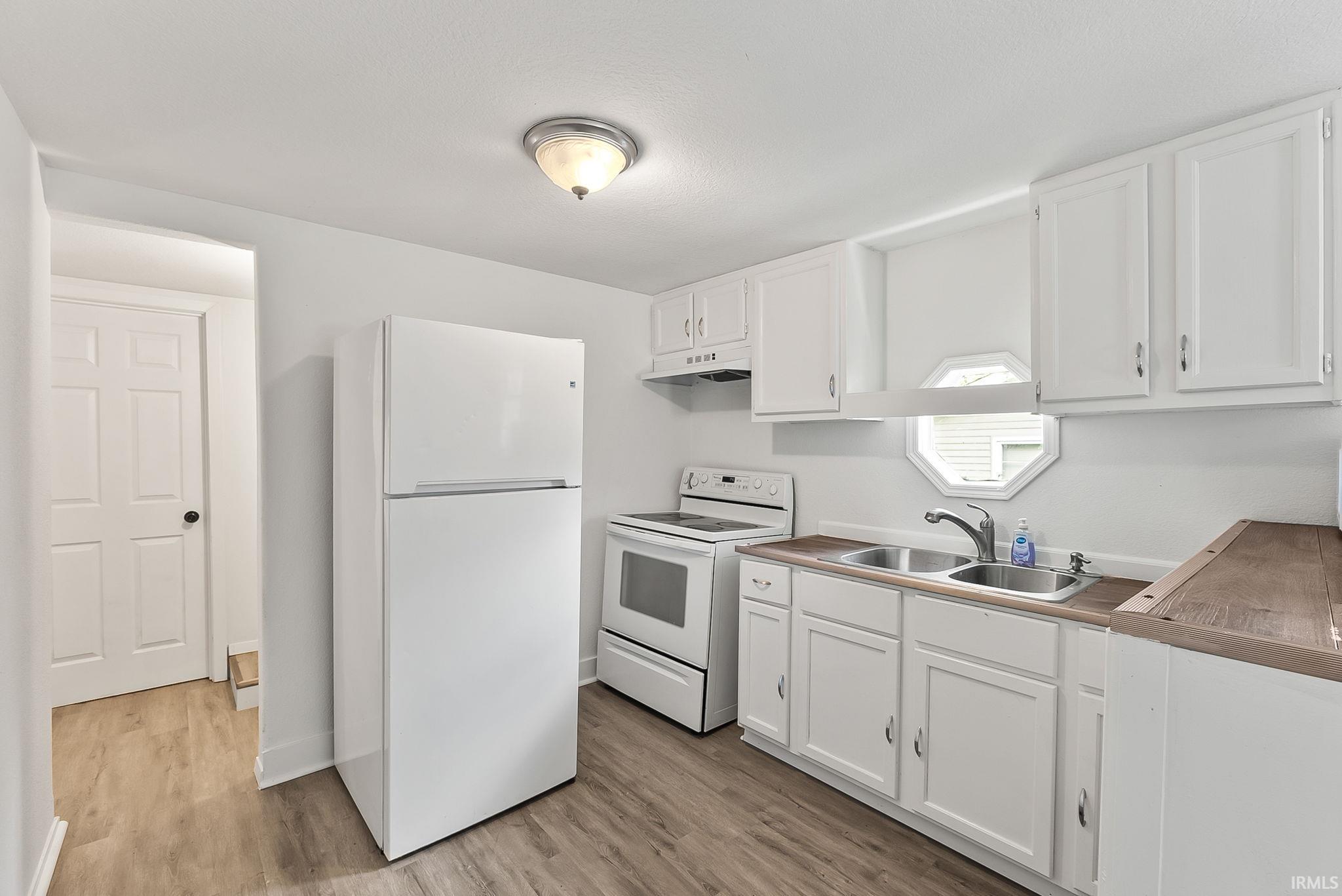 Kitchen featuring white cabinetry, wood-finish countertops, stainless steel double basin sink, and a white appliance package