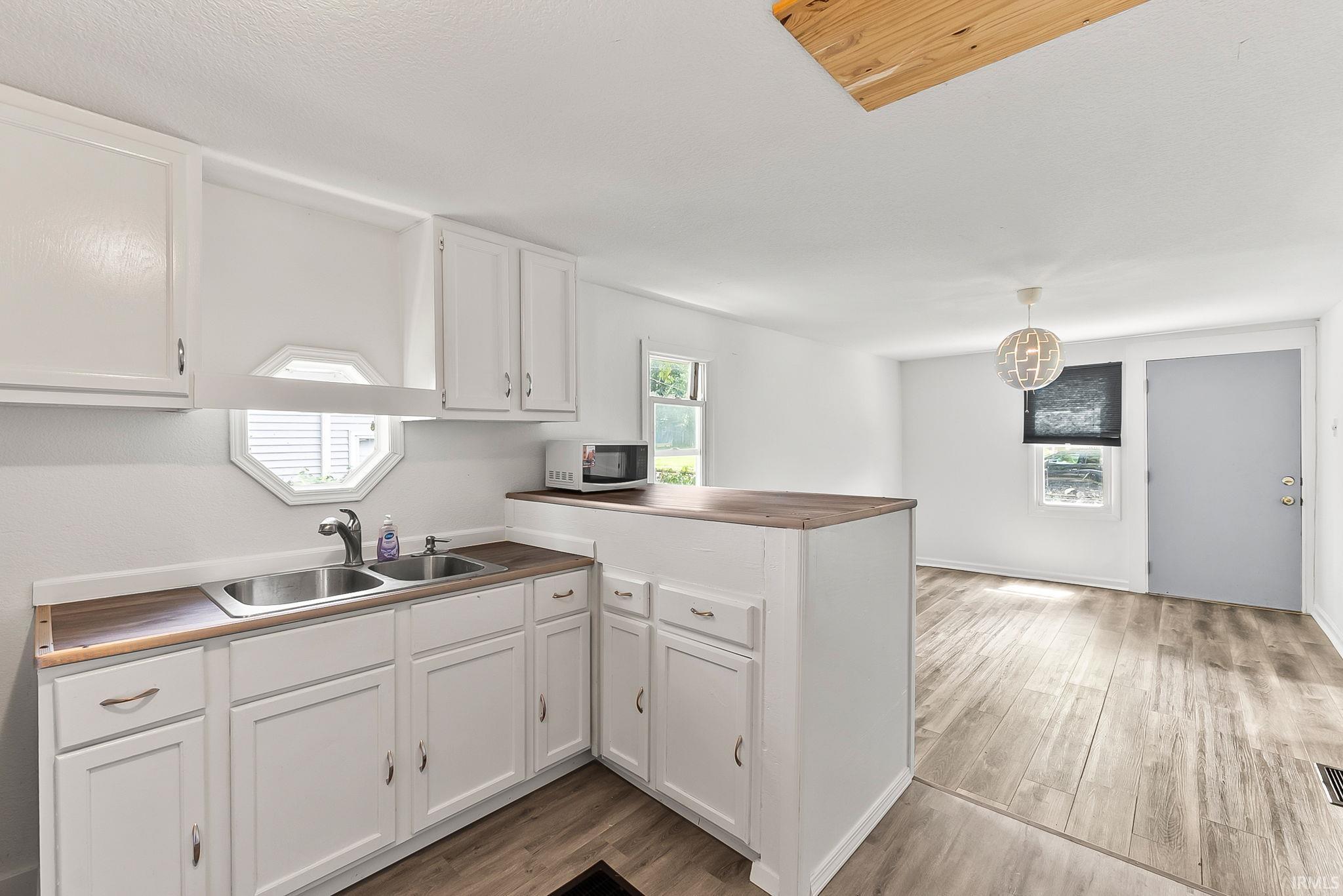 White cabinetry with wood-finish countertops, dual basin stainless steel sink, and wood-finish flooring