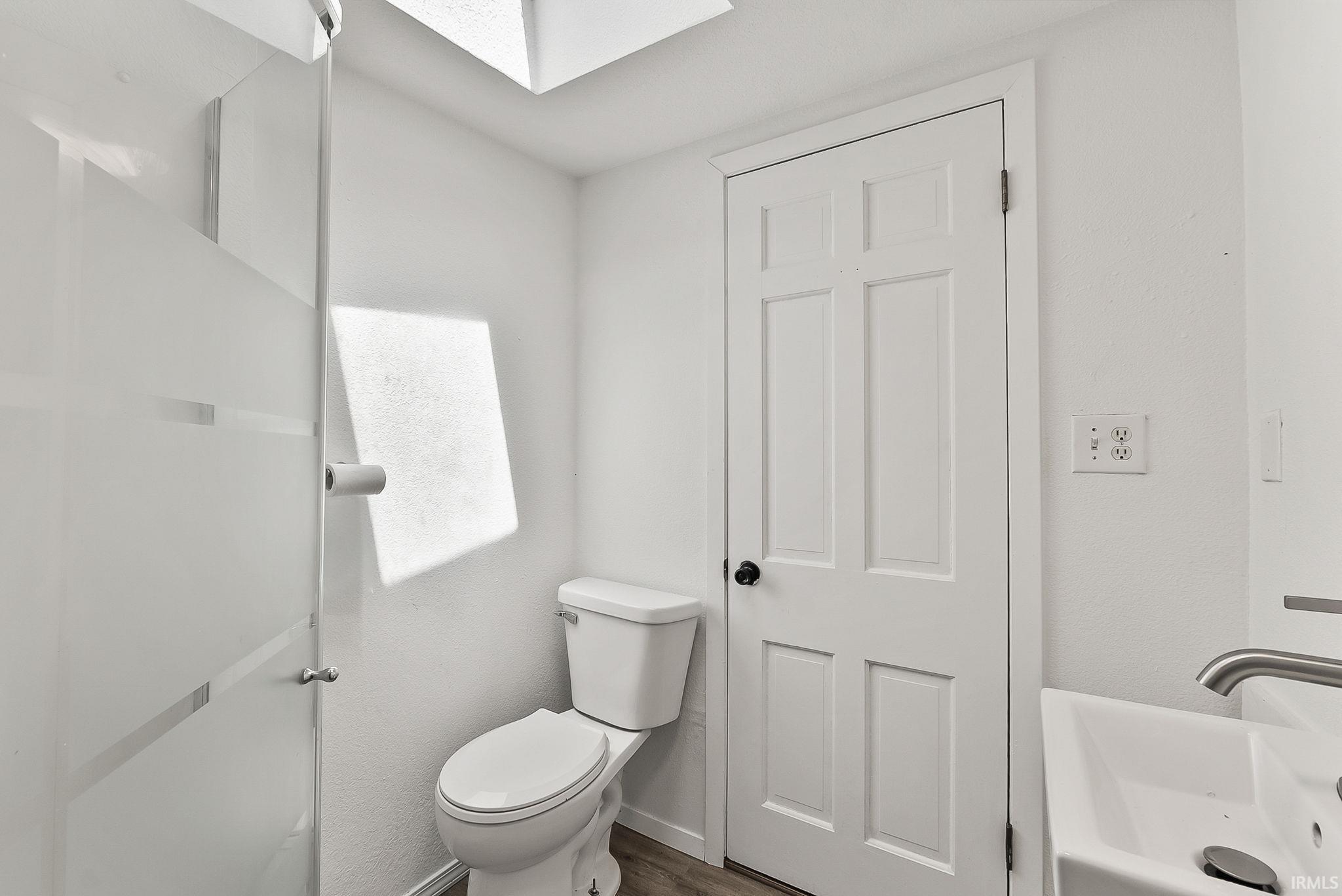 White bathroom featuring a skylight, frosted glass shower enclosure, white paneled door, and a modern vessel sink with a brushed metal faucet