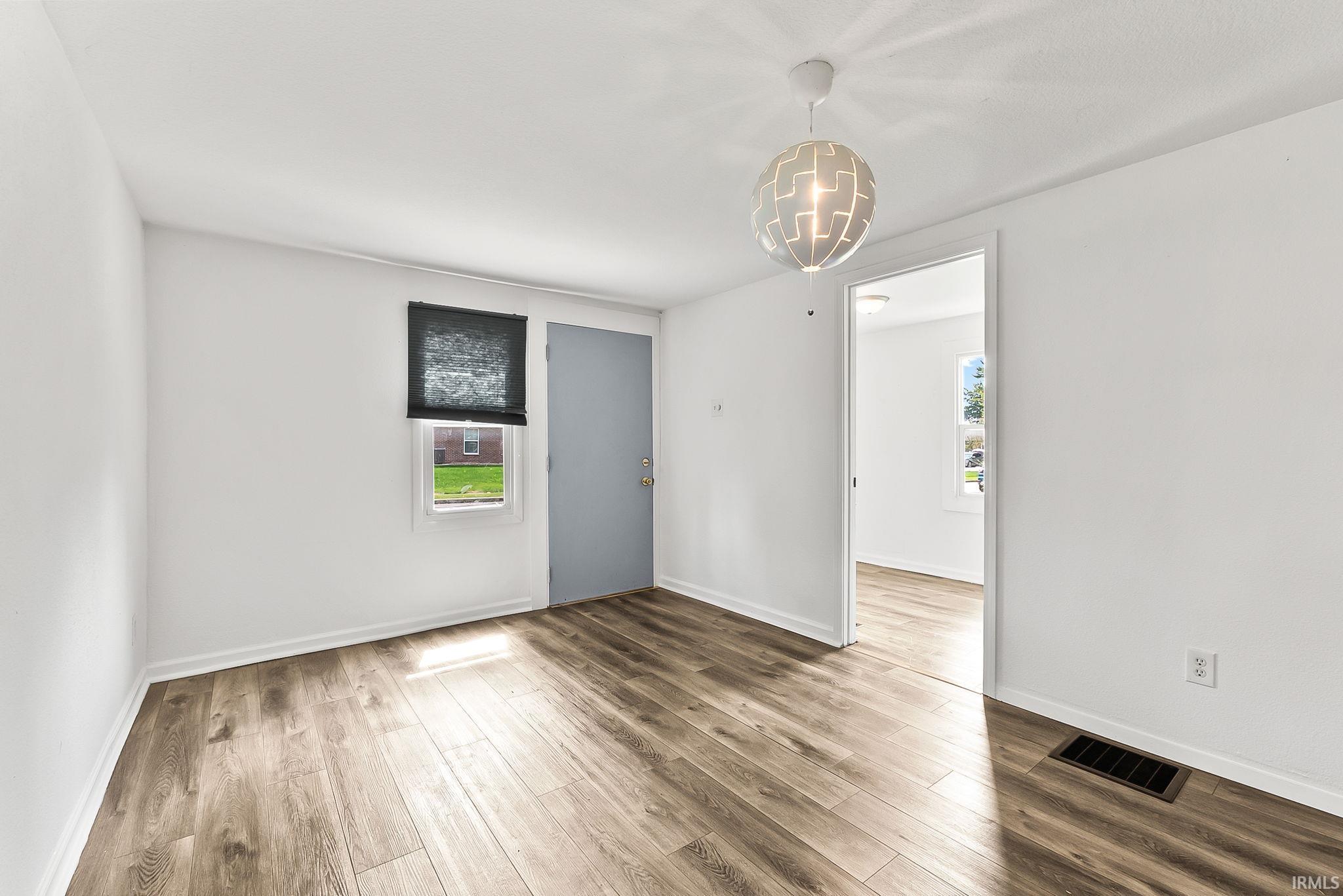 Wood-finish flooring, white painted walls, a modern pendant light fixture, and a window with a dark roller shade