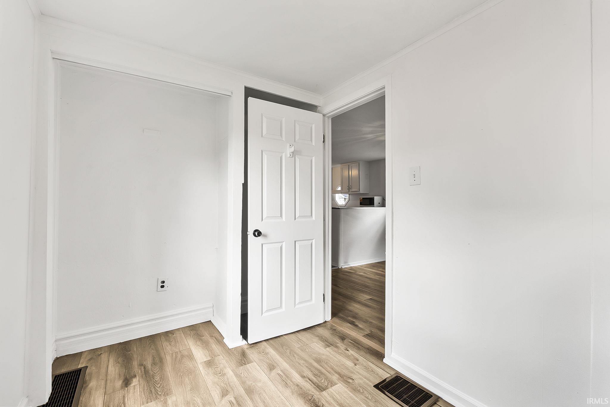 Wood-finish flooring throughout, white walls, and a paneled interior door