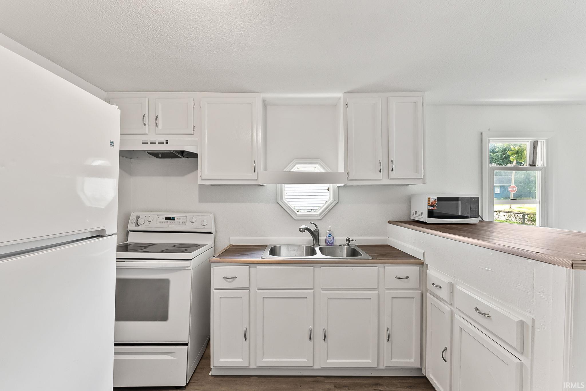 Kitchen featuring white cabinetry, wood-finish countertops, stainless steel double-basin sink, and a white electric range with an overhead vent