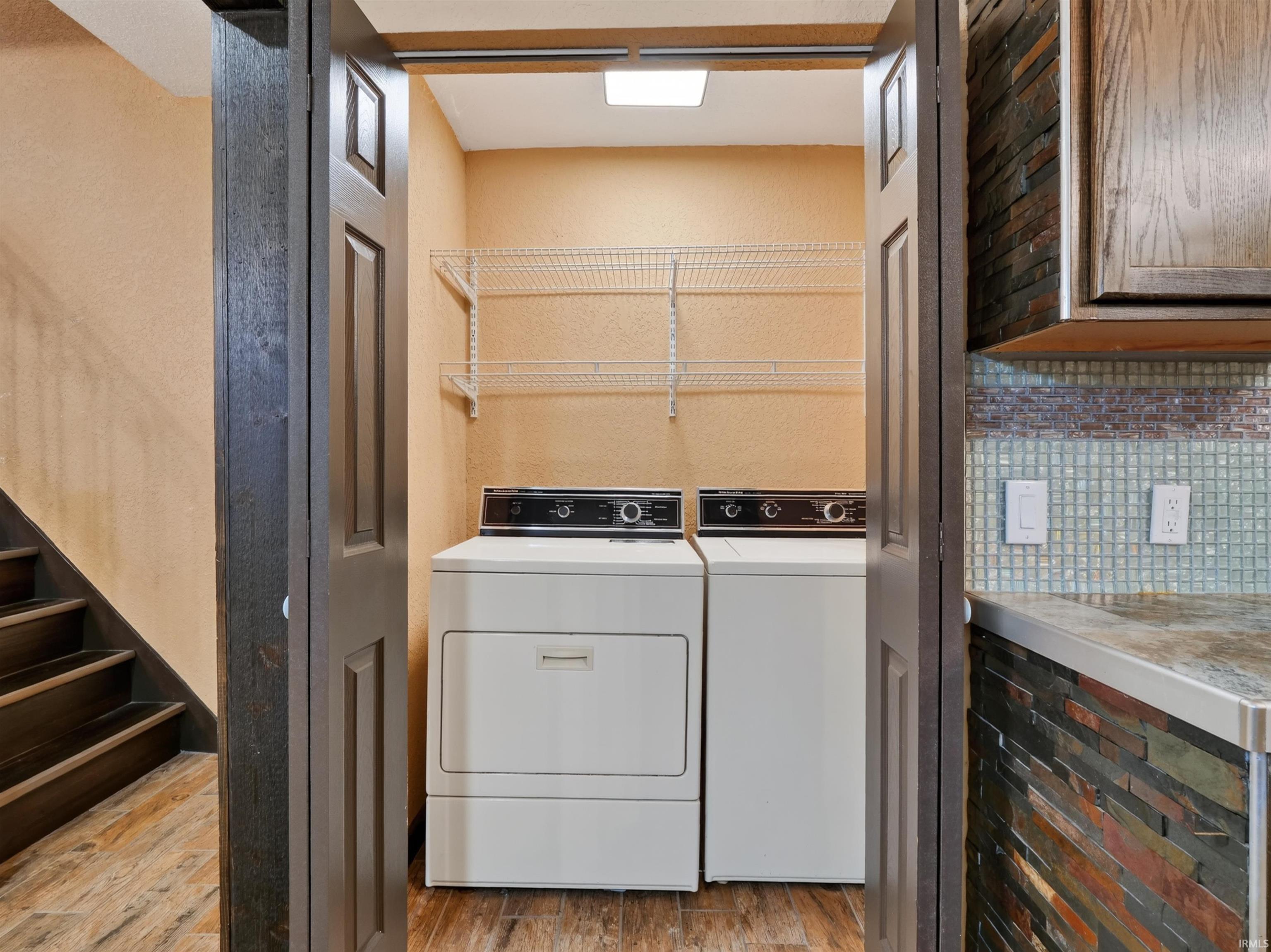 Utility area with wood-finish flooring, included appliances, wire shelving, and overhead lighting