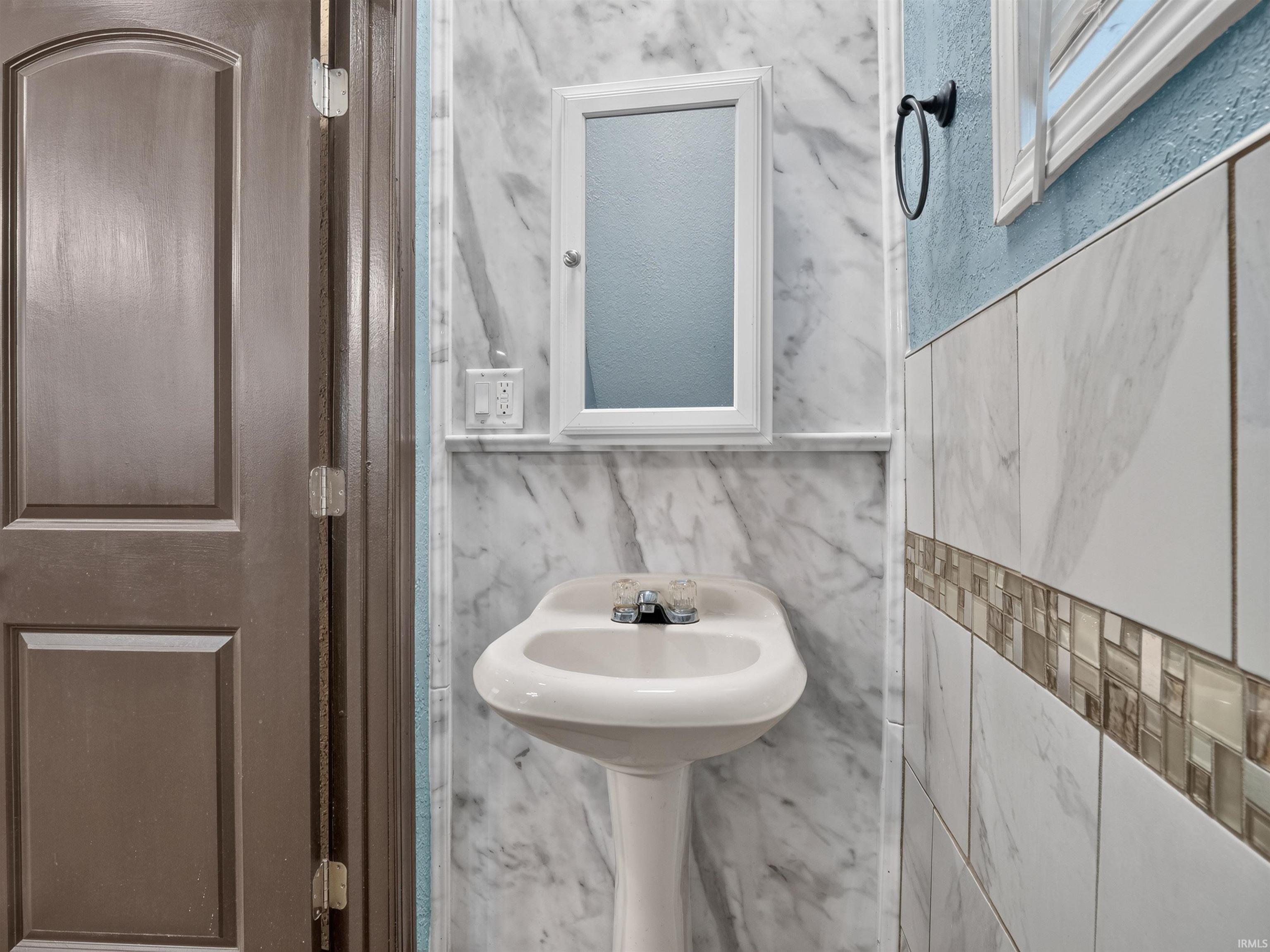 Pedestal sink with chrome faucet, complemented by a white-framed medicine cabinet