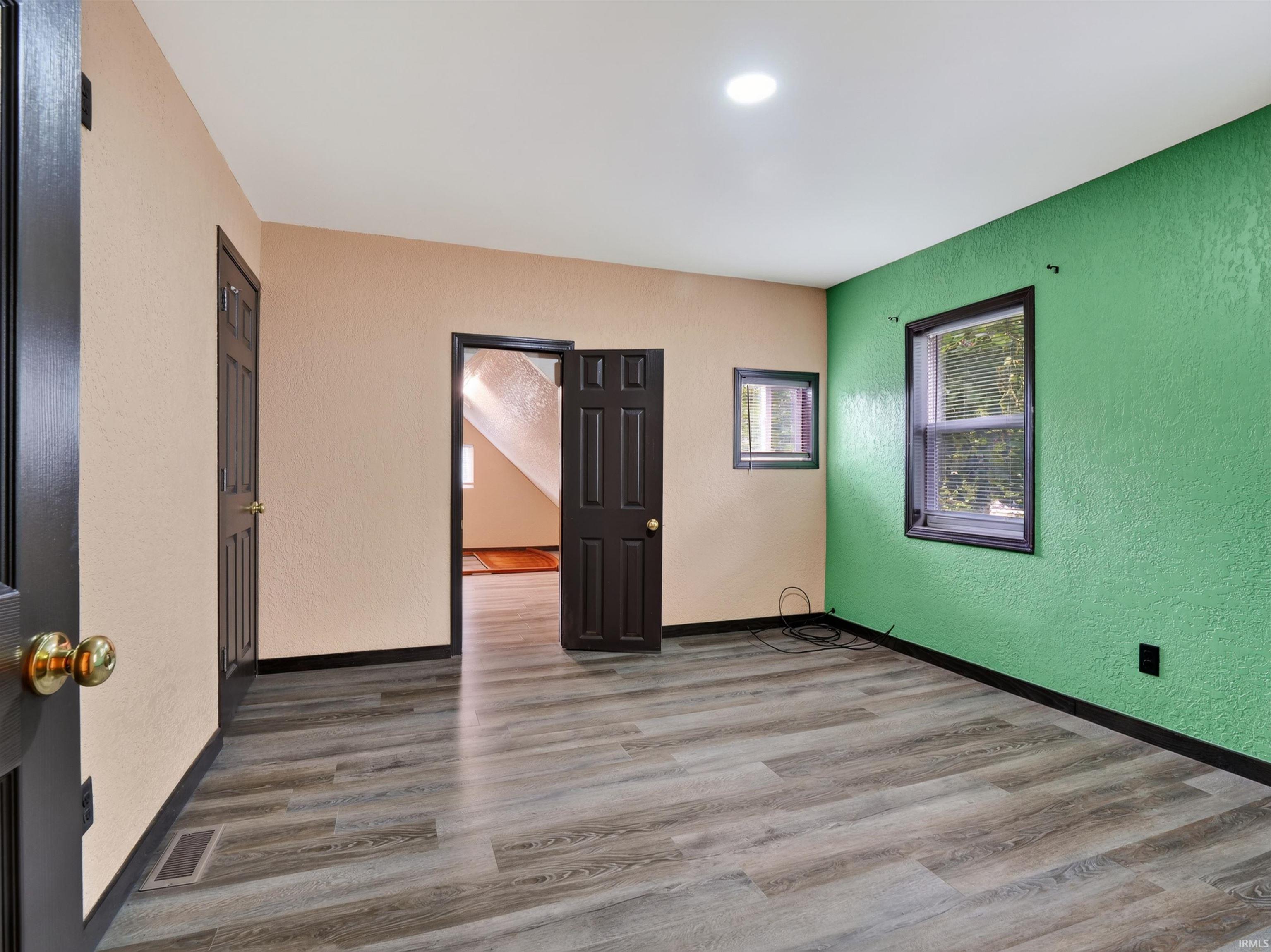 Wood-finish flooring with black baseboards, two panel doors, and recessed lighting