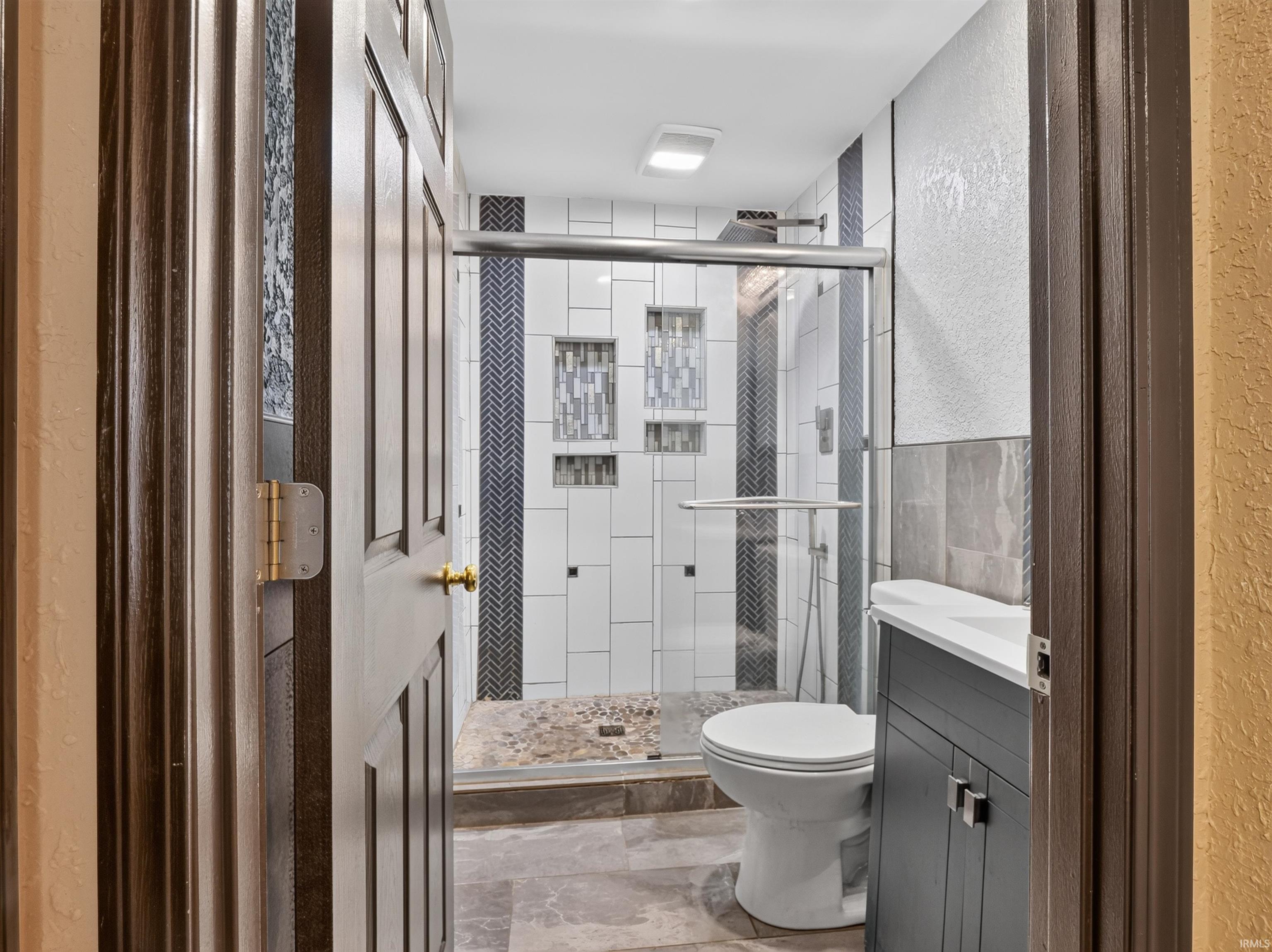 Walk-in shower with glass enclosure, white tile surround, and accent tiling