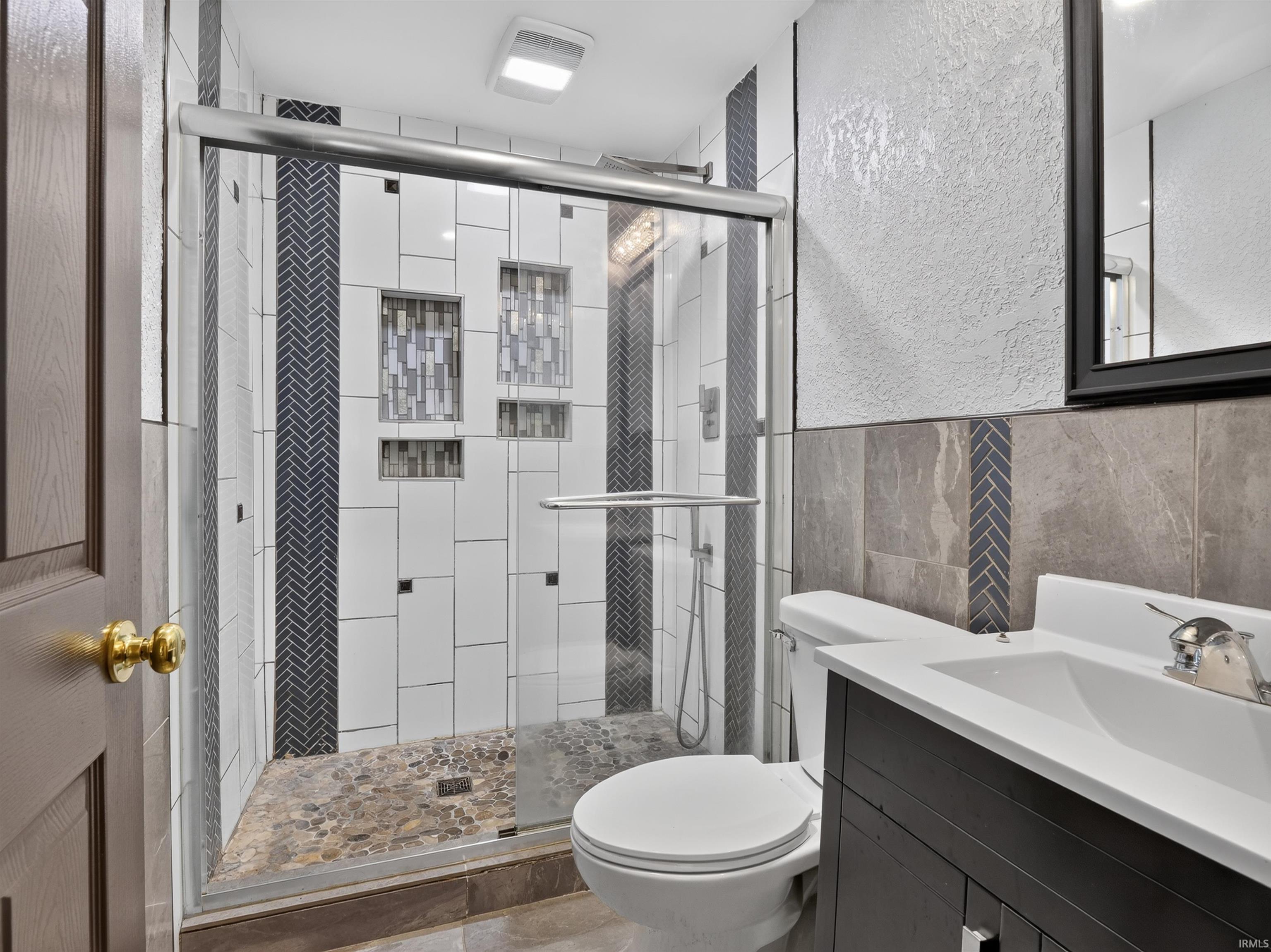 Walk-in shower with clear glass enclosure, decorative tile accents, and built-in shelving