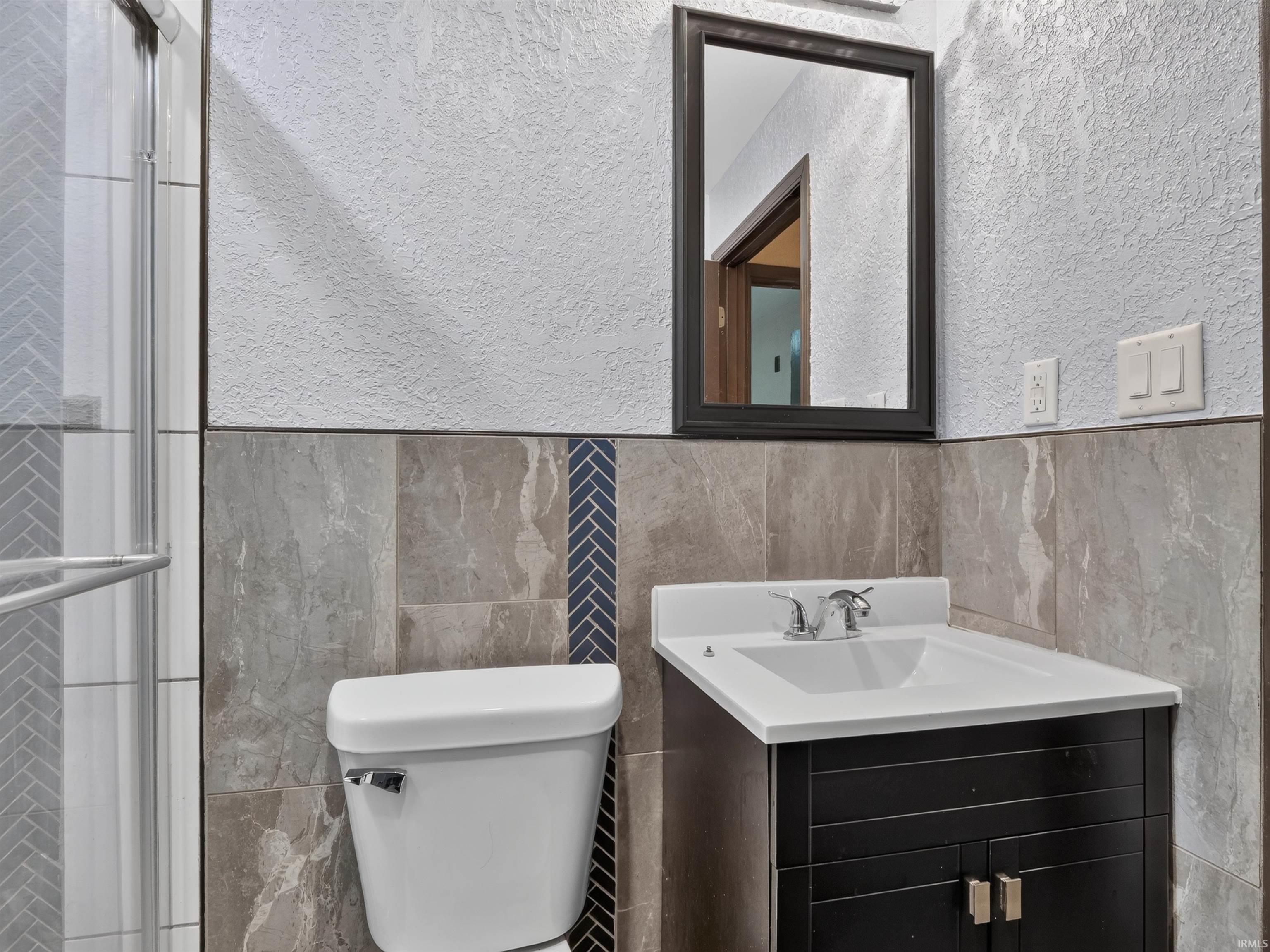 Vanity with integrated sink, framed mirror, and tiled walls with decorative herringbone accent