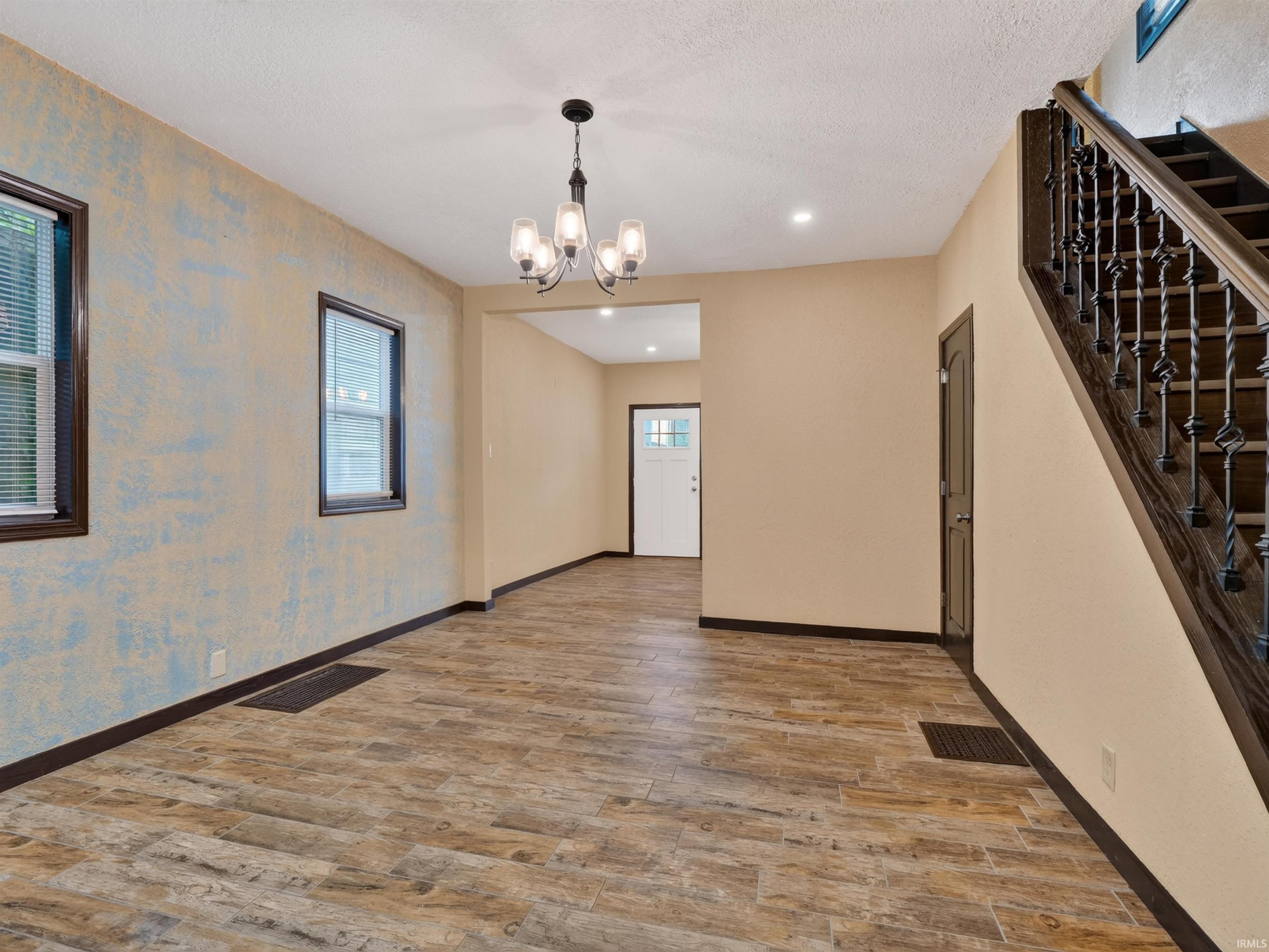 Wood-finish flooring, dark wood trim, classic chandelier, wrought iron staircase balusters, and multiple windows
