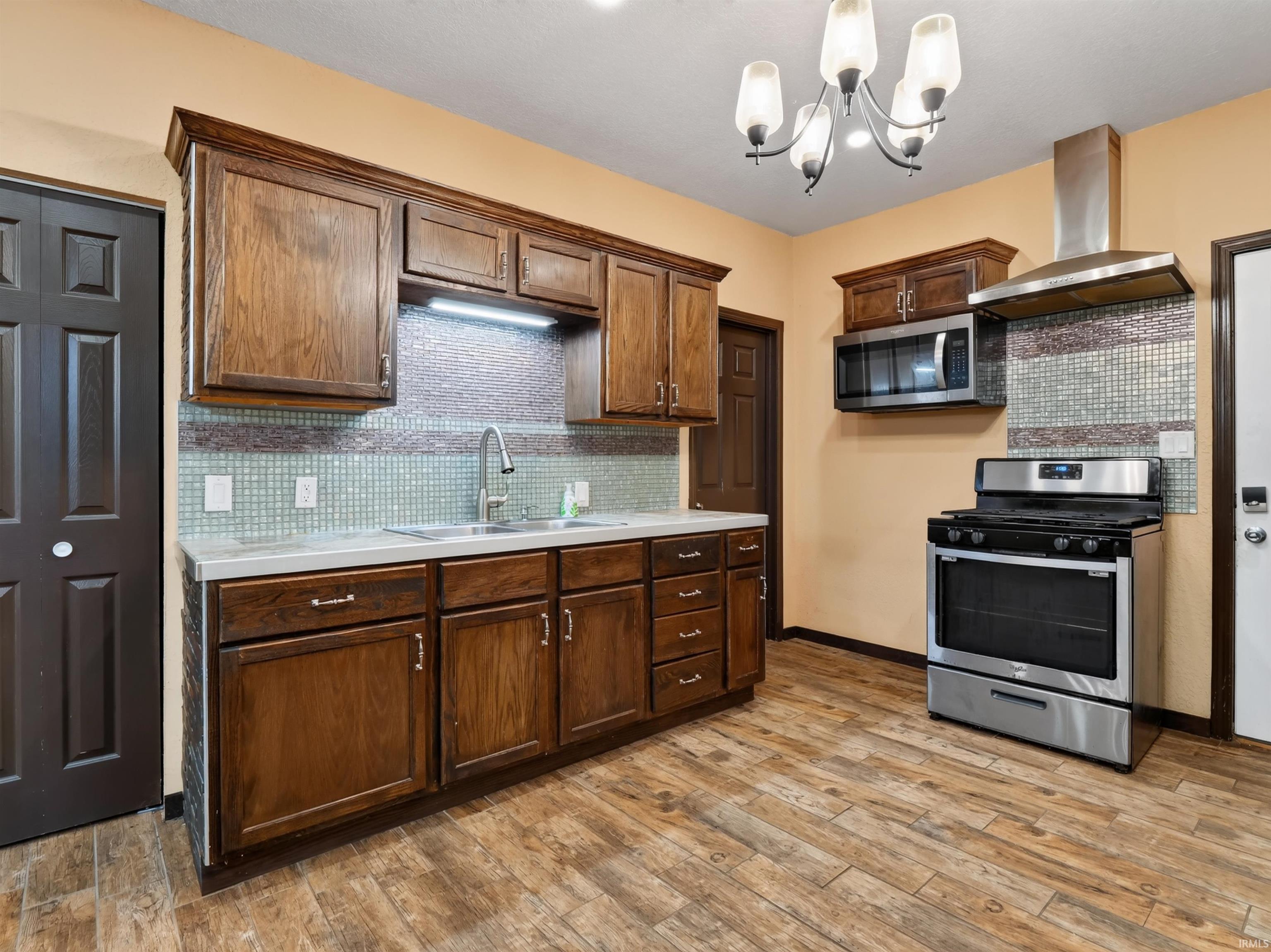 Kitchen featuring wood-finish flooring, stainless steel range with overhead microwave, wood cabinetry, and mosaic tile backsplash