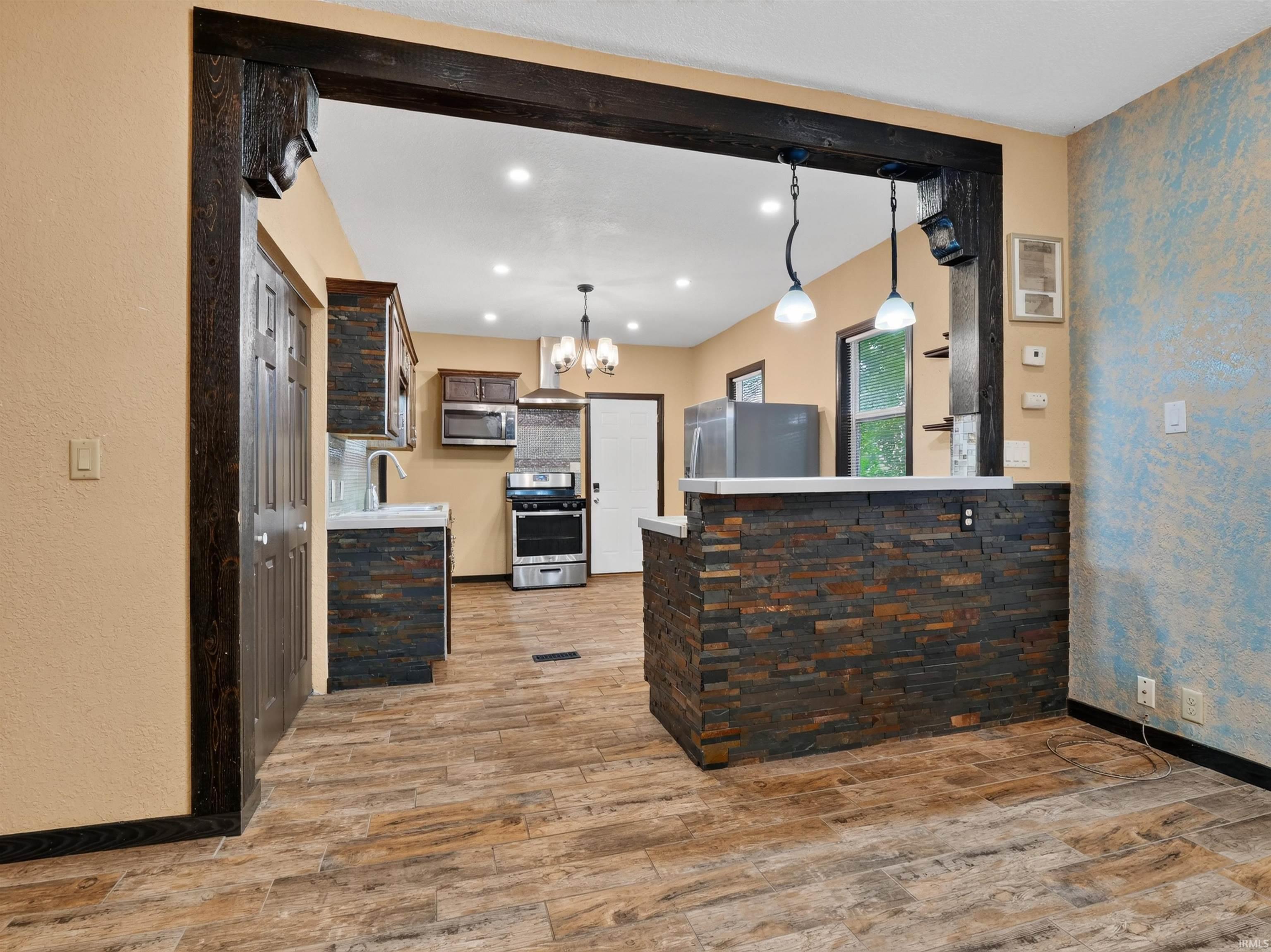 Kitchen featuring wood-finish flooring, stainless steel appliances, recessed lighting, stone-clad breakfast bar, and wood-toned cabinetry