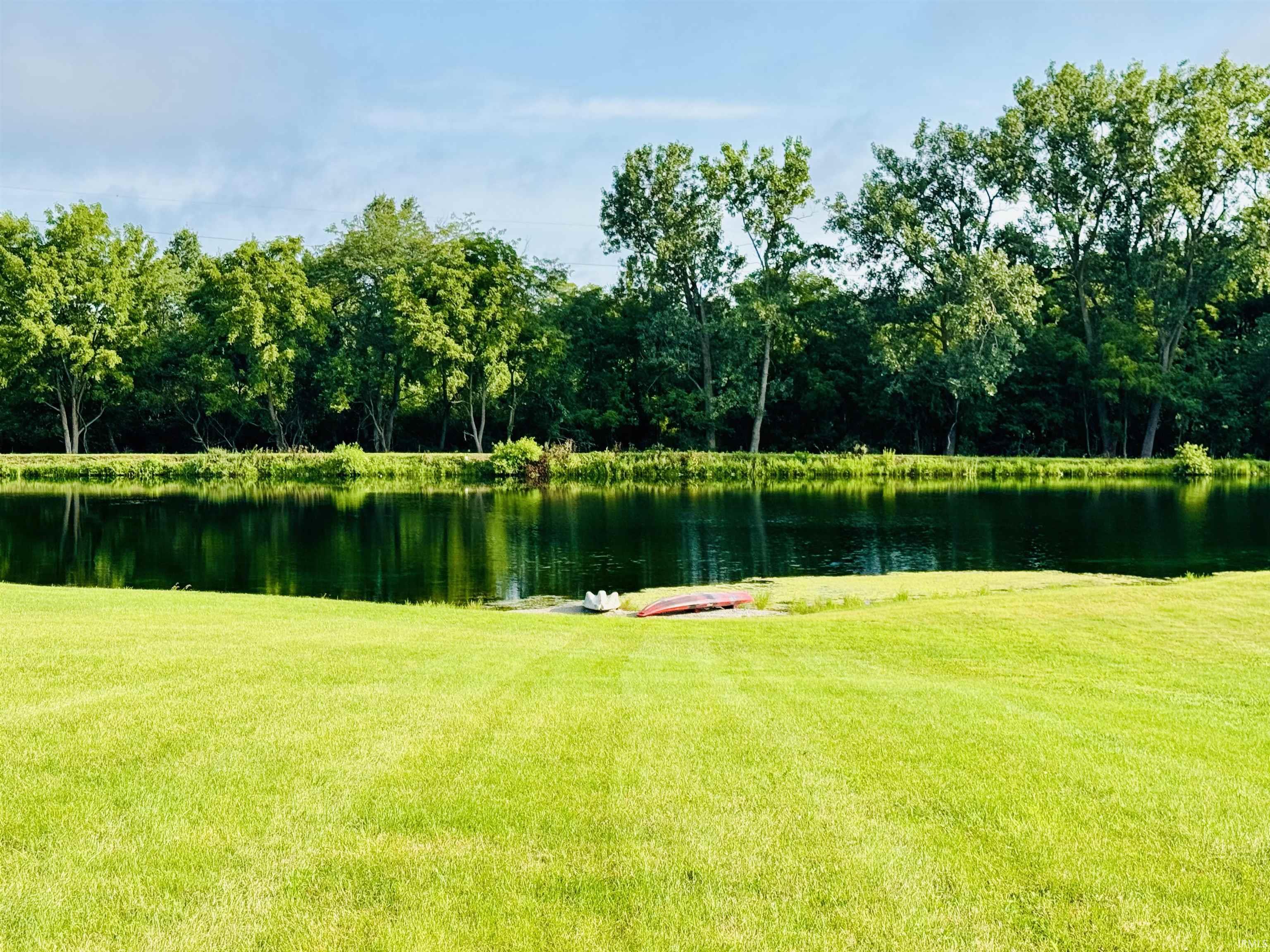 Grassed lawn leading to a private pond with wooded surroundings